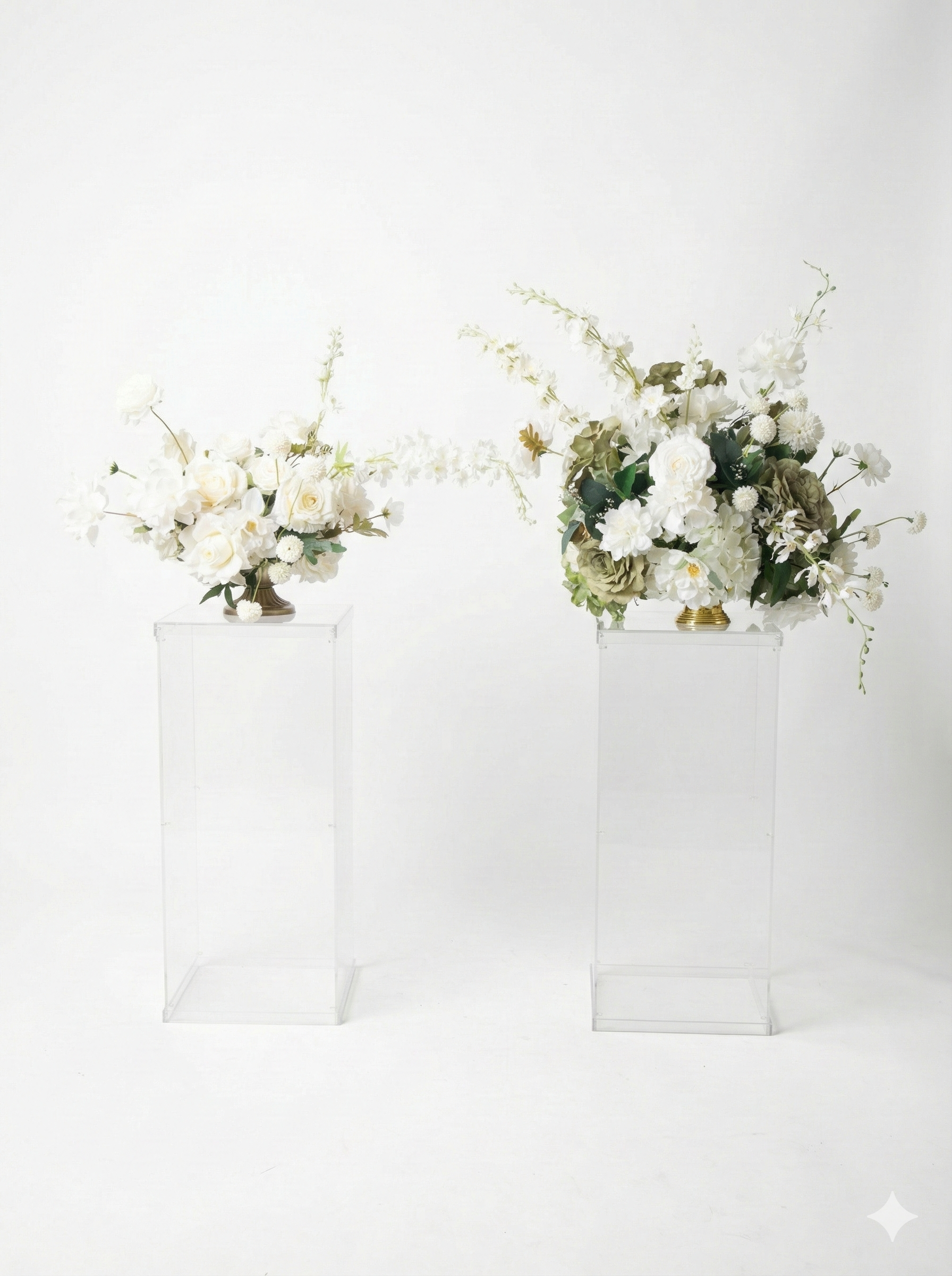 Two floral arrangements in white vases on clear rectangular pedestals, featuring white roses, hydrangeas, and other white flowers.