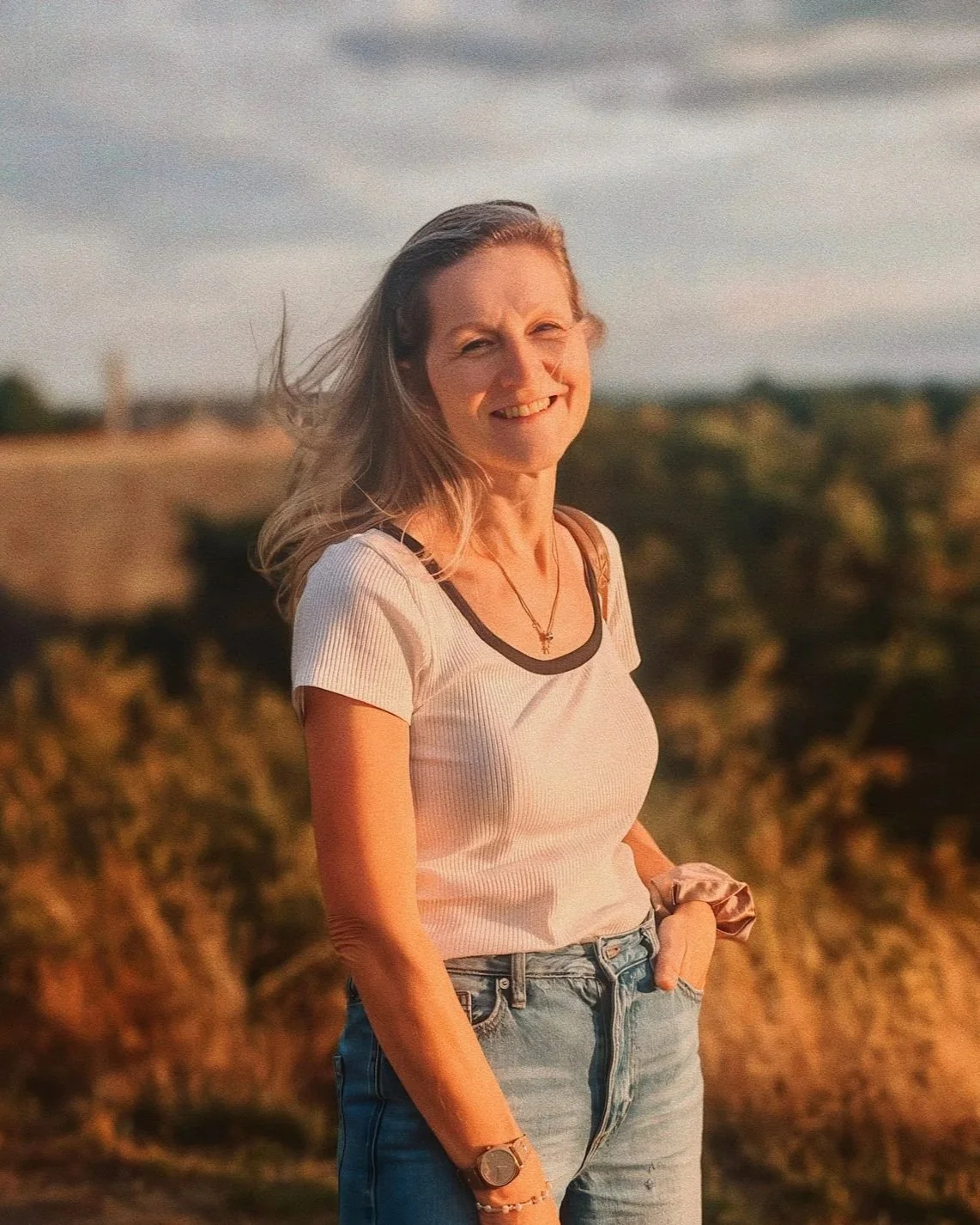 Woman smiling outdoors at sunset in casual clothing, representing confidence, balance, and everyday wellness living.