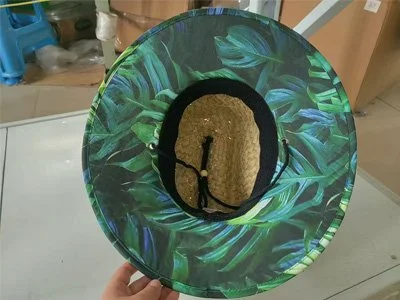 A person holding a round mirror with a tropical leaf design frame, reflecting the ceiling.