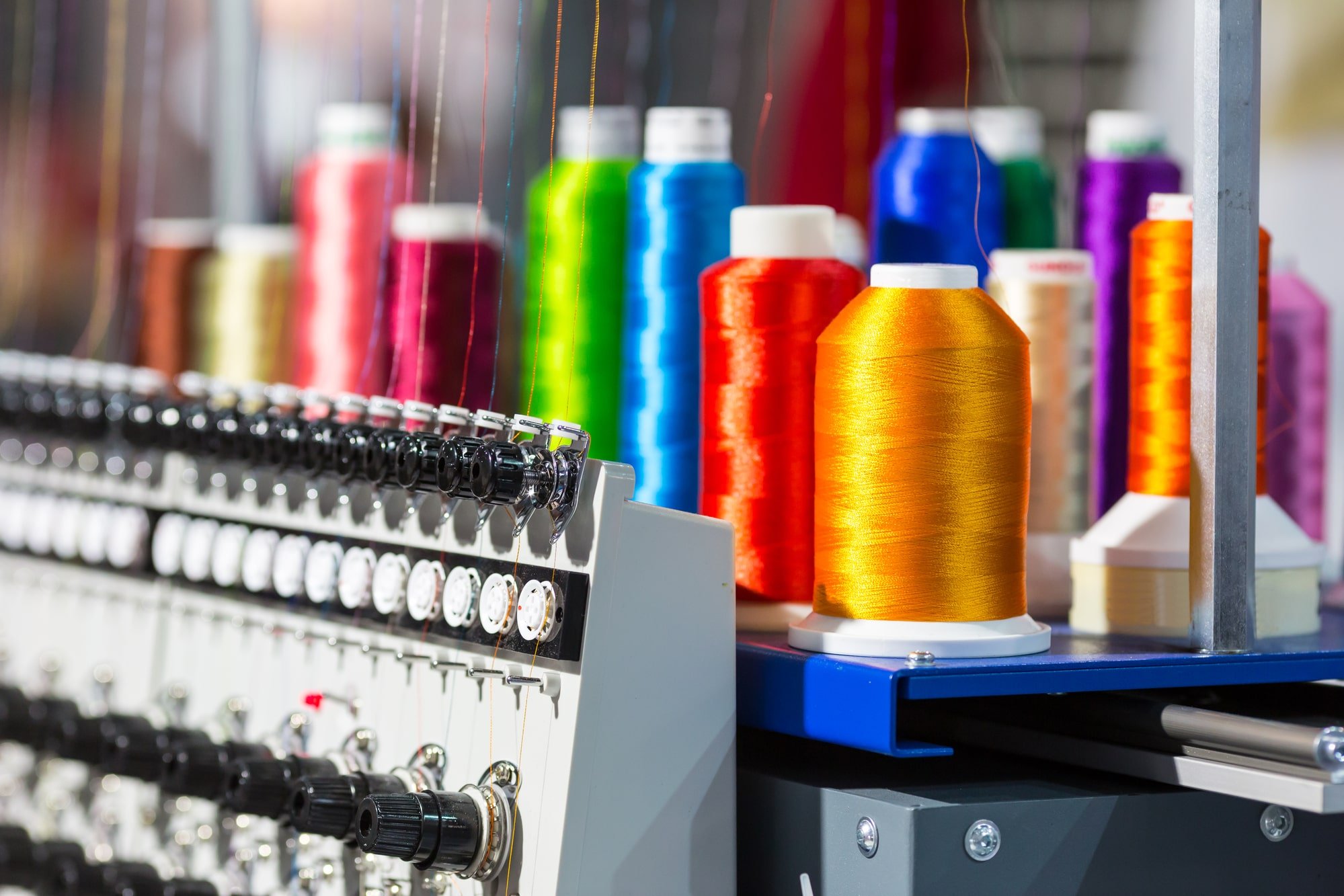 Spools of colorful thread on a sewing machine, with thread colors including red, orange, yellow, green, blue, purple, and pink.