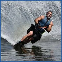 Man wearing a sleeveless shirt and sunglasses riding a surfboard through the water