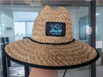 A wide-brimmed straw hat with a black border and a black patch that reads "Hang 10 Car Wash" in blue lettering.