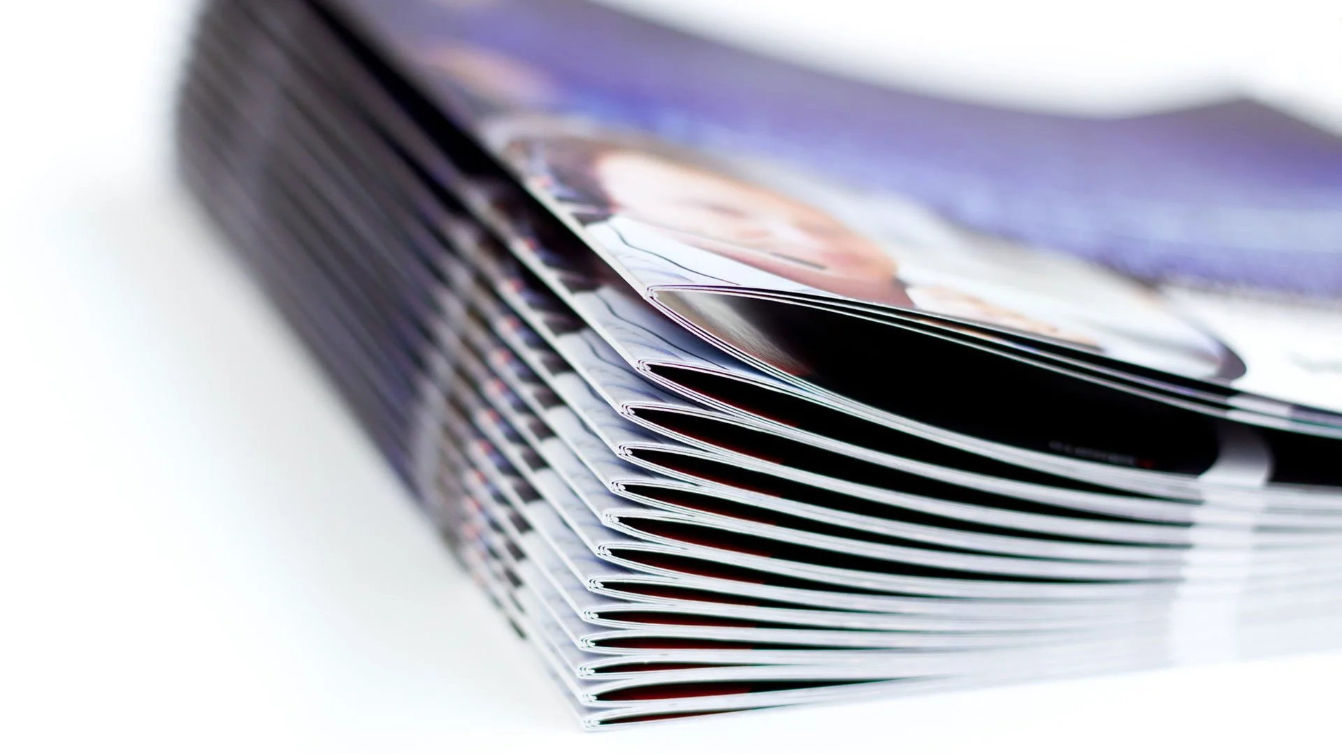 Close-up of a stack of glossy magazines, slightly fanned out, showing colorful pages and photographs.