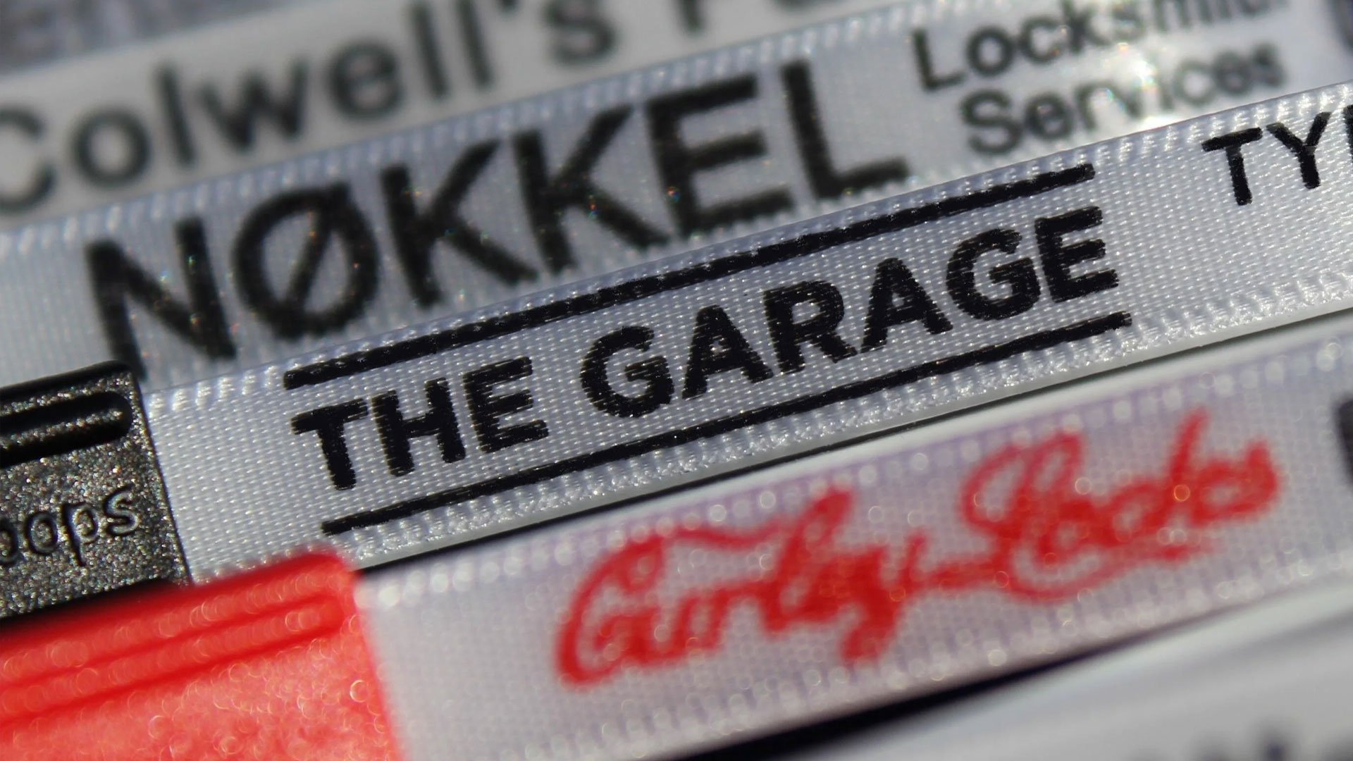 Close-up of a label on a product package with the text 'THE GARAGE' underlined and part of the words 'NOOKEL' and 'The' visible, with red cursive handwriting at the bottom.