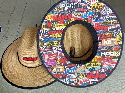 A straw cowboy hat with a colorful stickered brim, placed on a gray surface.