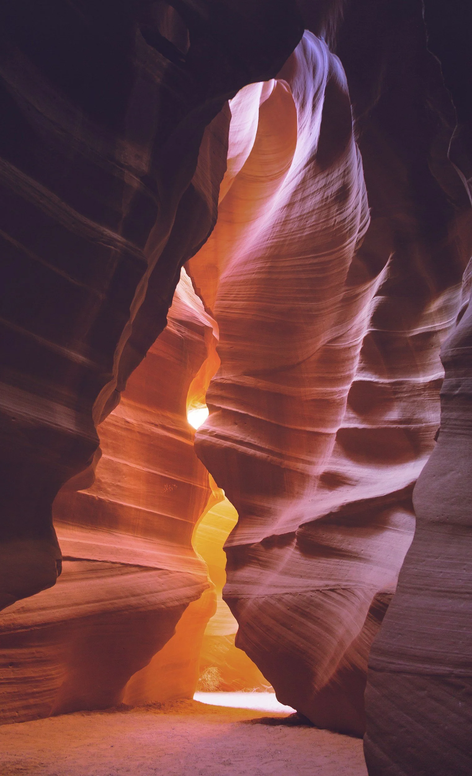 Narrow slot canyon with smooth, colorful sandstone walls illuminated by sunlight from above.