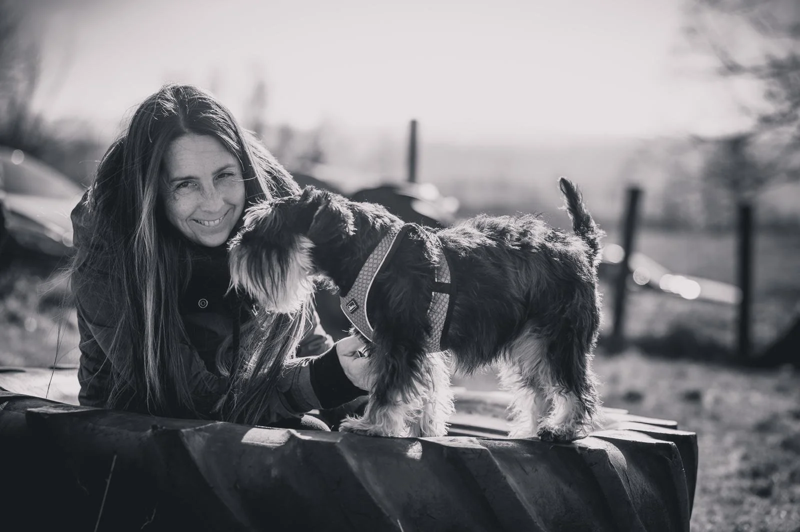 Frau lächelt, während sie mit ihrem Hund draußen spielt.