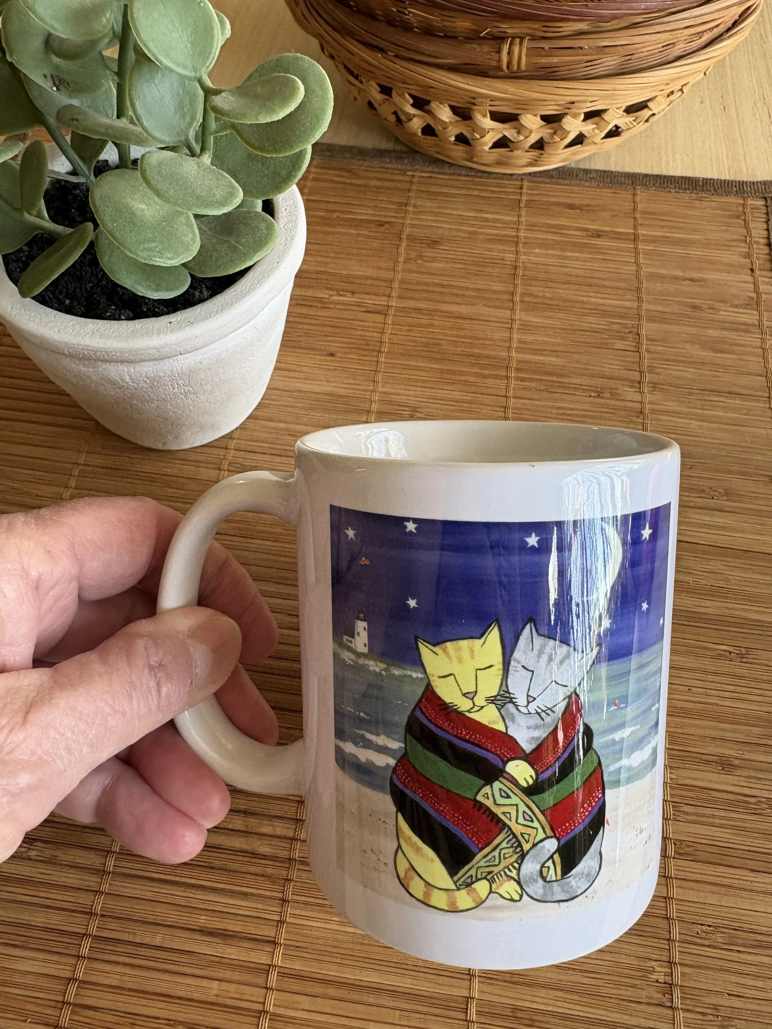 Photo of Jen Niles Art mug featuring painting called Beachtowel Cats with a succulent plant and basket in the background