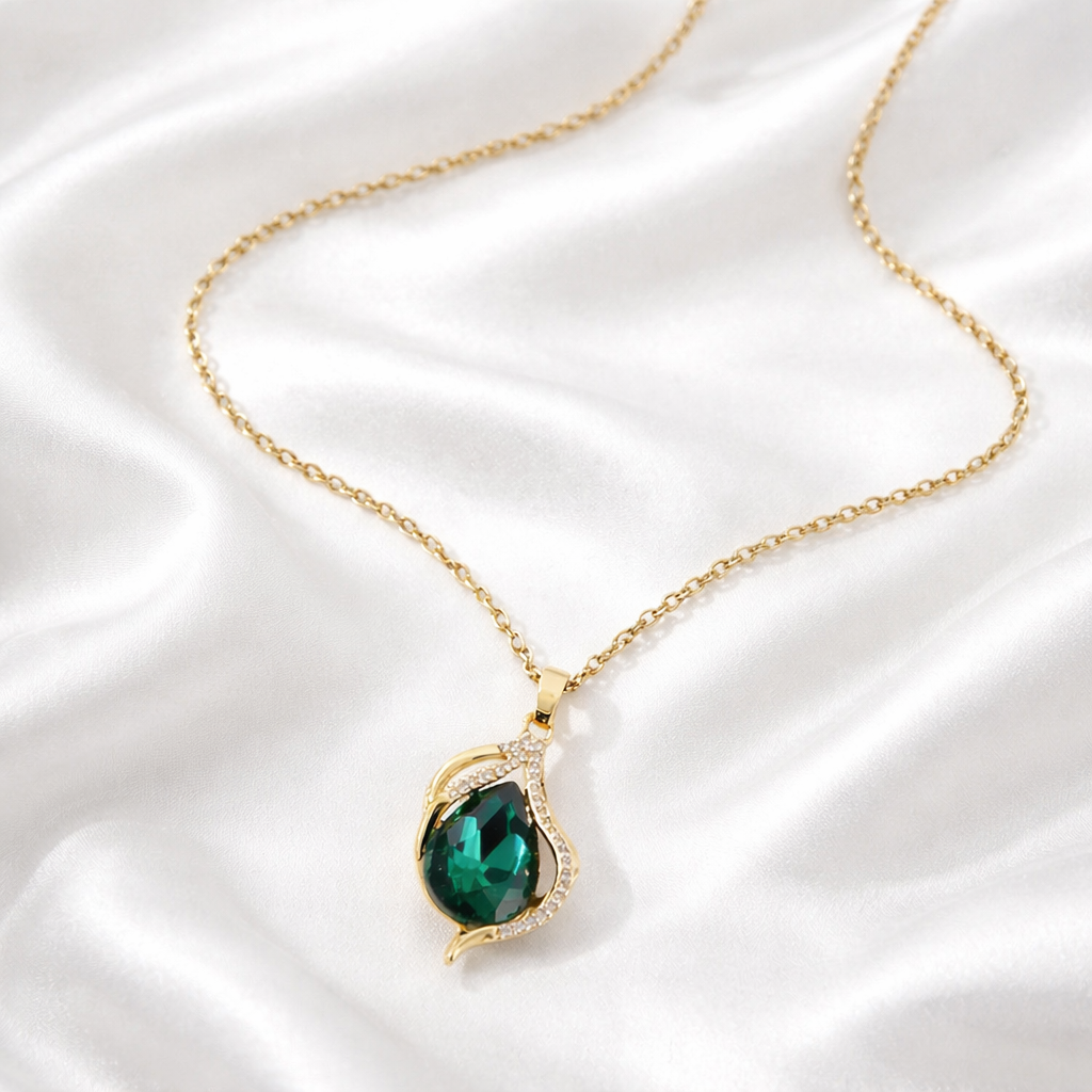 Gold necklace with a green gemstone pendant on white satin fabric.