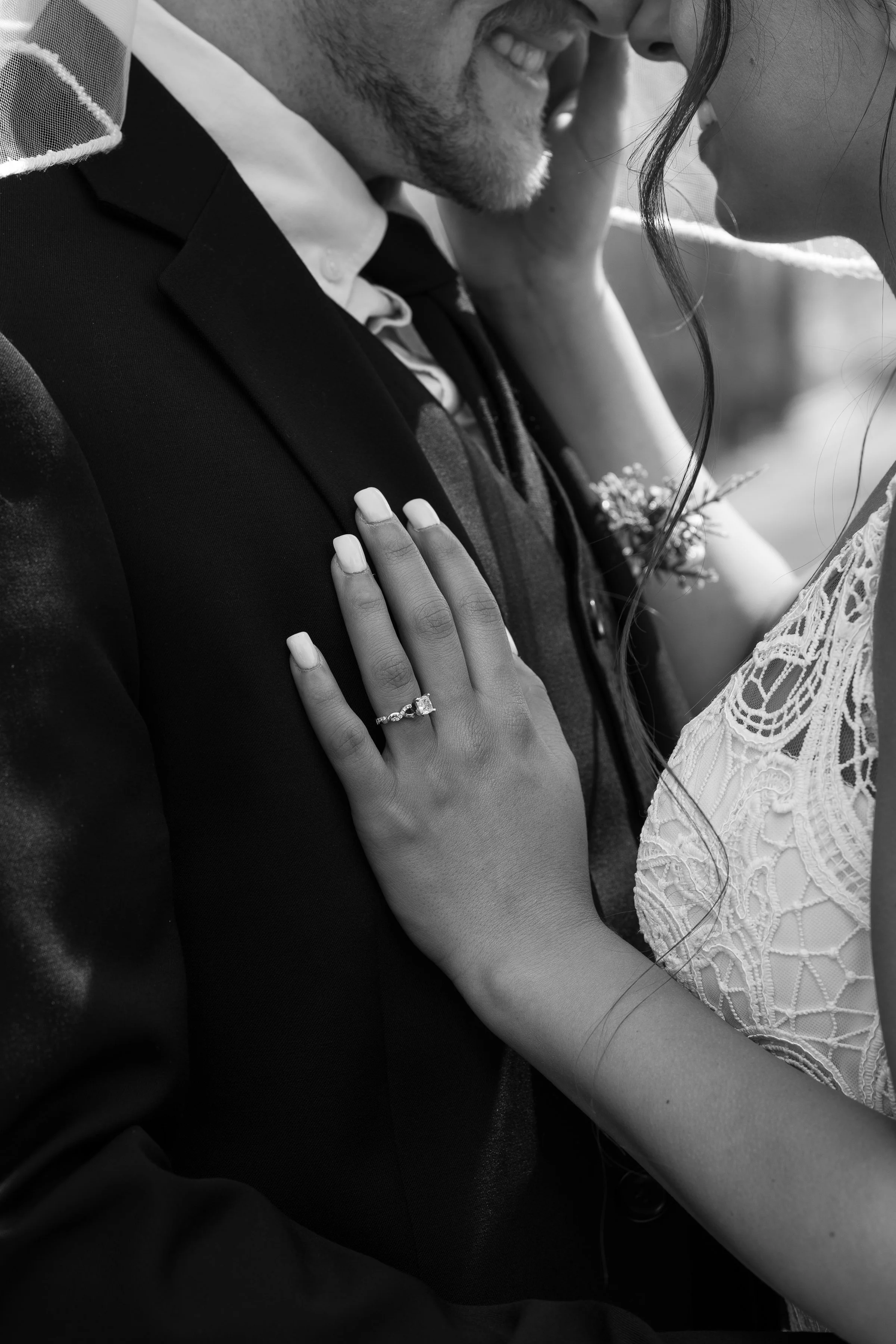 Close-up of a bride and groom sharing an intimate moment, she touches his face, and he smiles, focusing on her hand with an engagement ring.