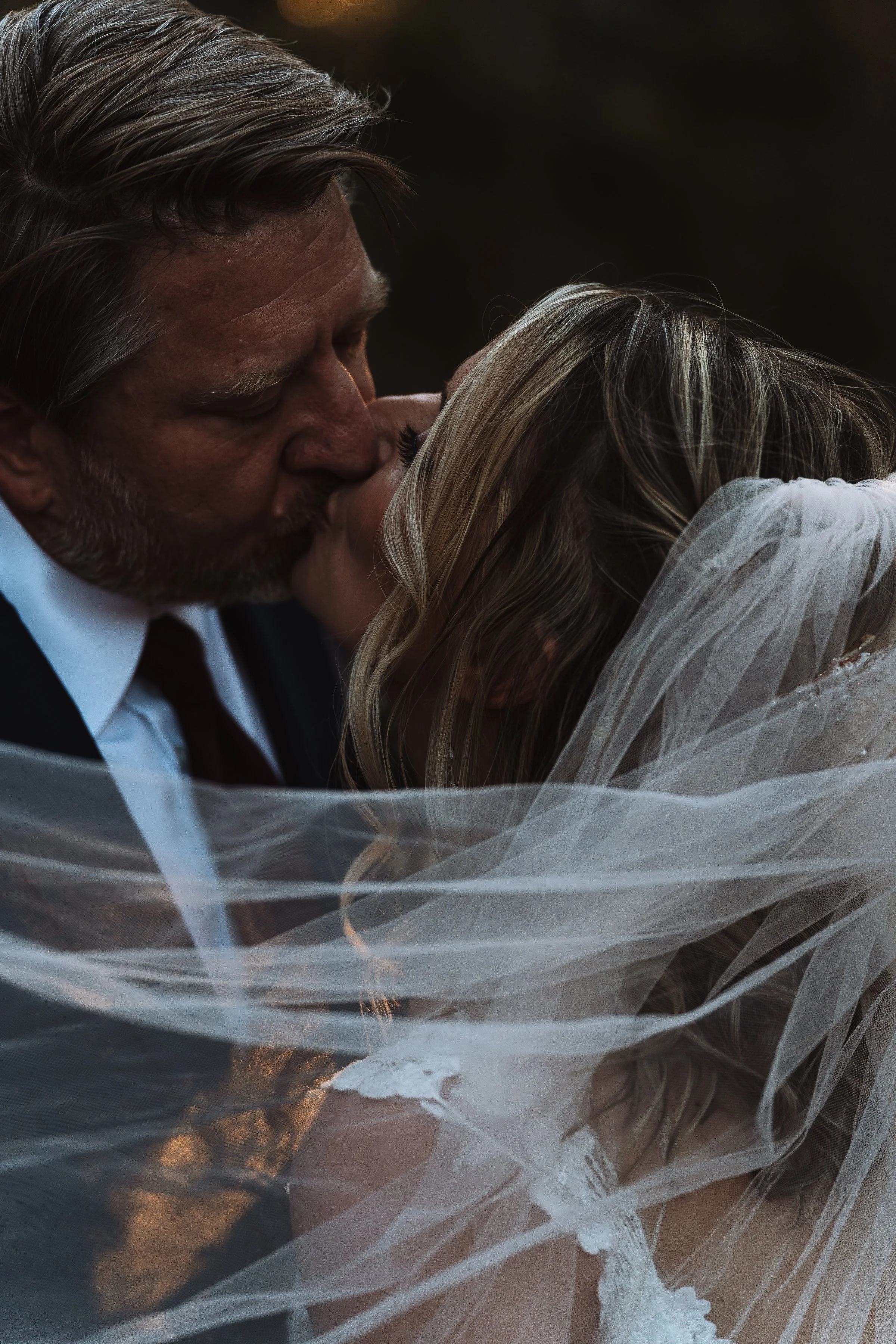 A man and woman are sharing a close, intimate kiss, with the woman wearing a wedding veil.
