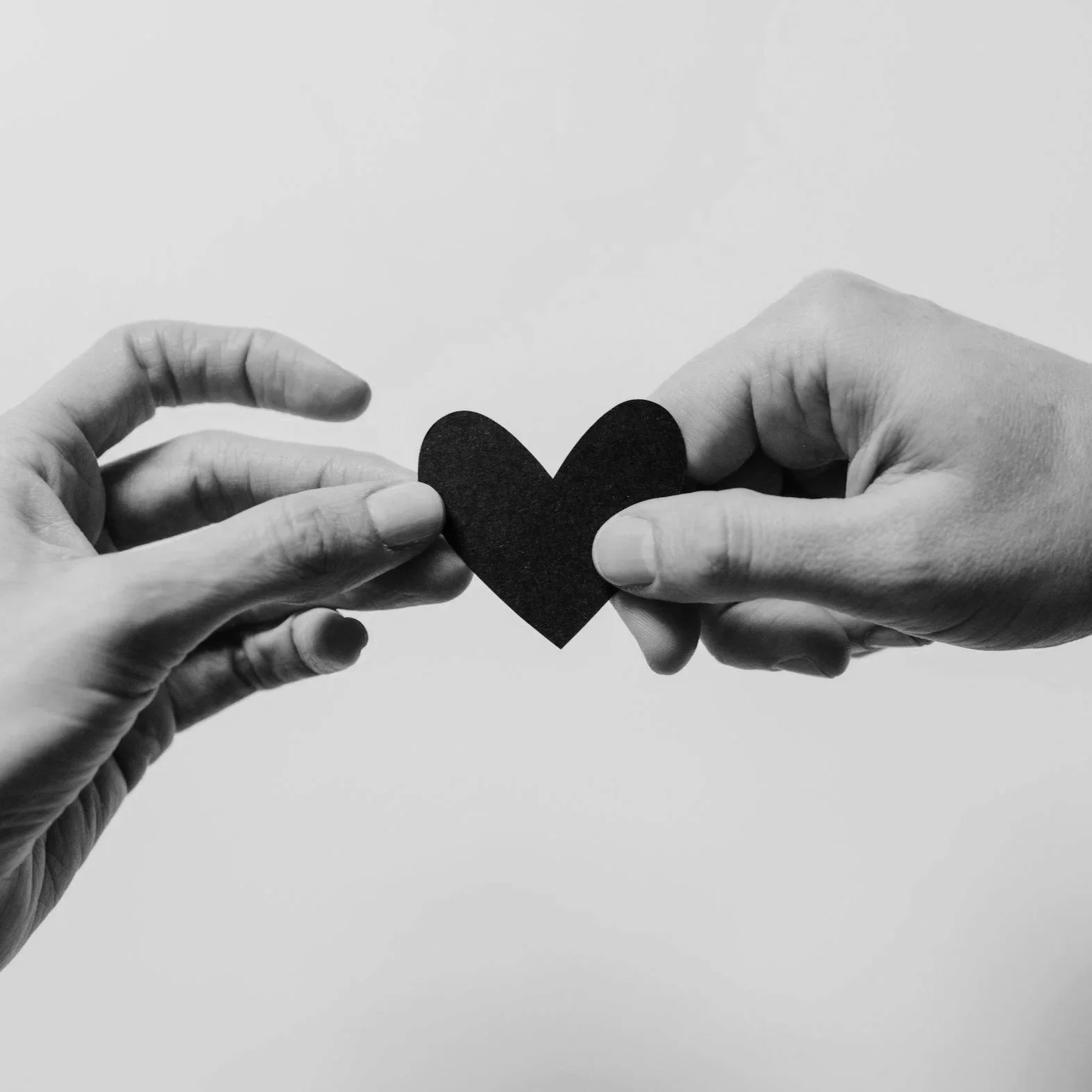 Two hands exchanging a small black heart cutout in black and white