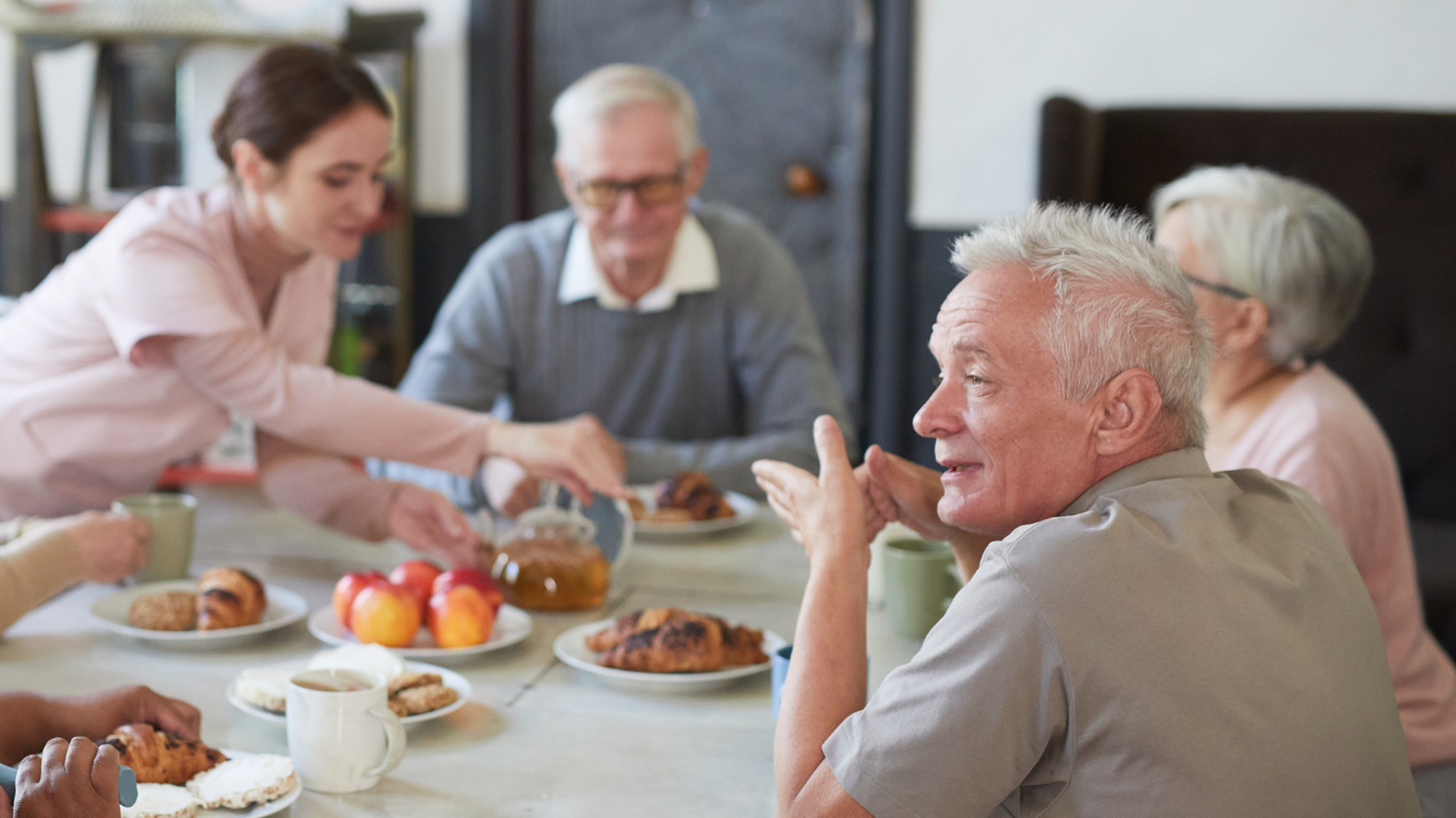 Group of elderly people having breakfast together at a dining table with food and drinks.