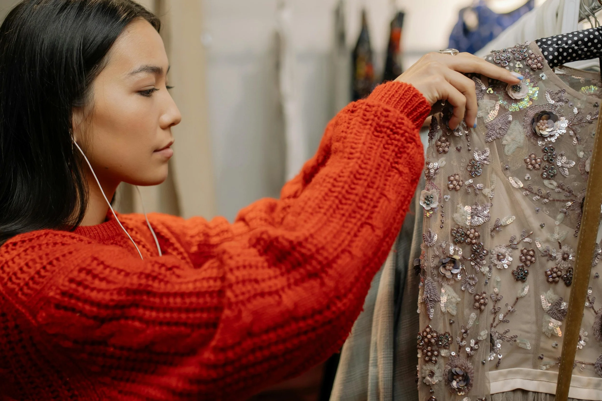 Woman wearing and orange sweater shopping for a dress.