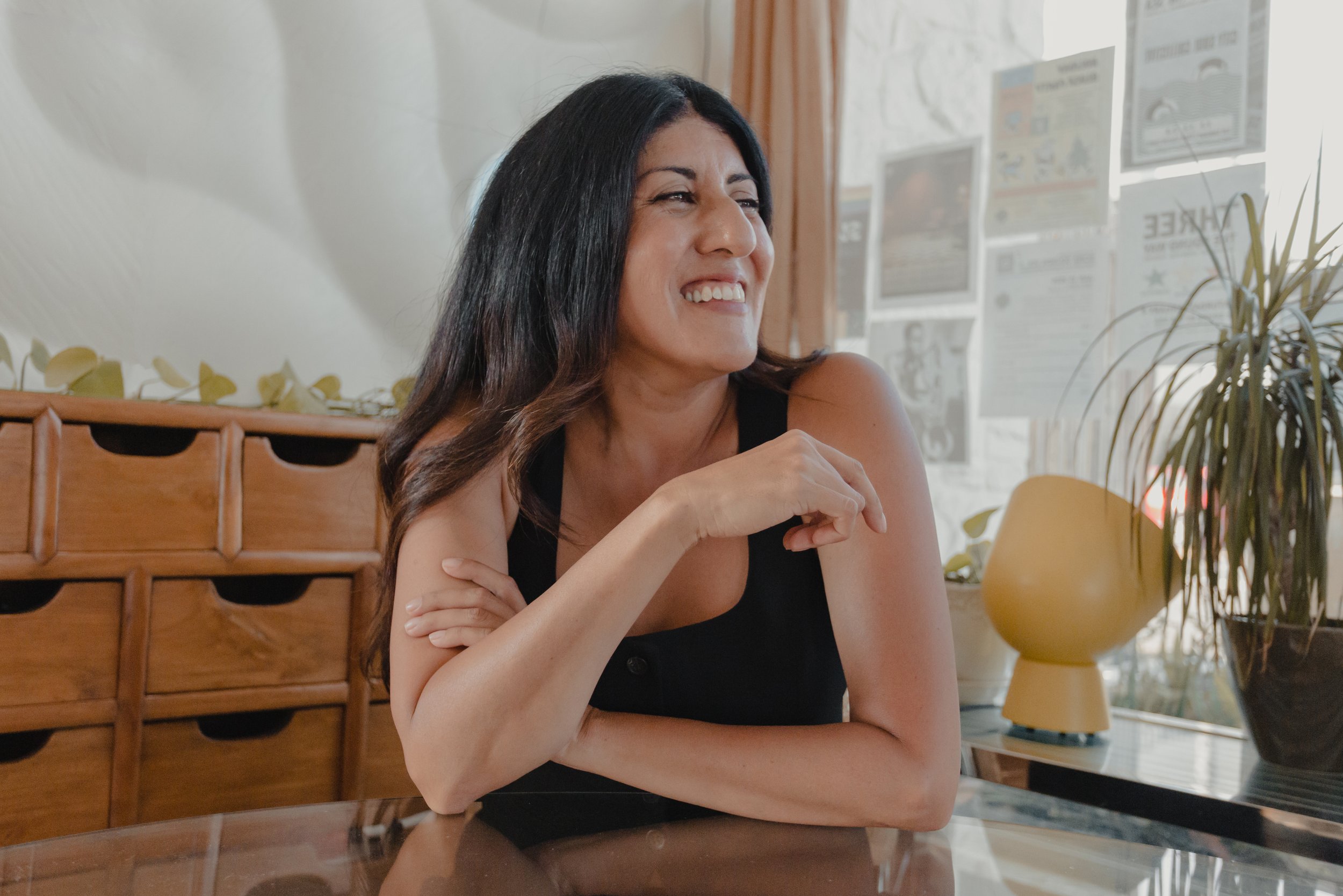 Woman with long hair sitting at a table and smiling.