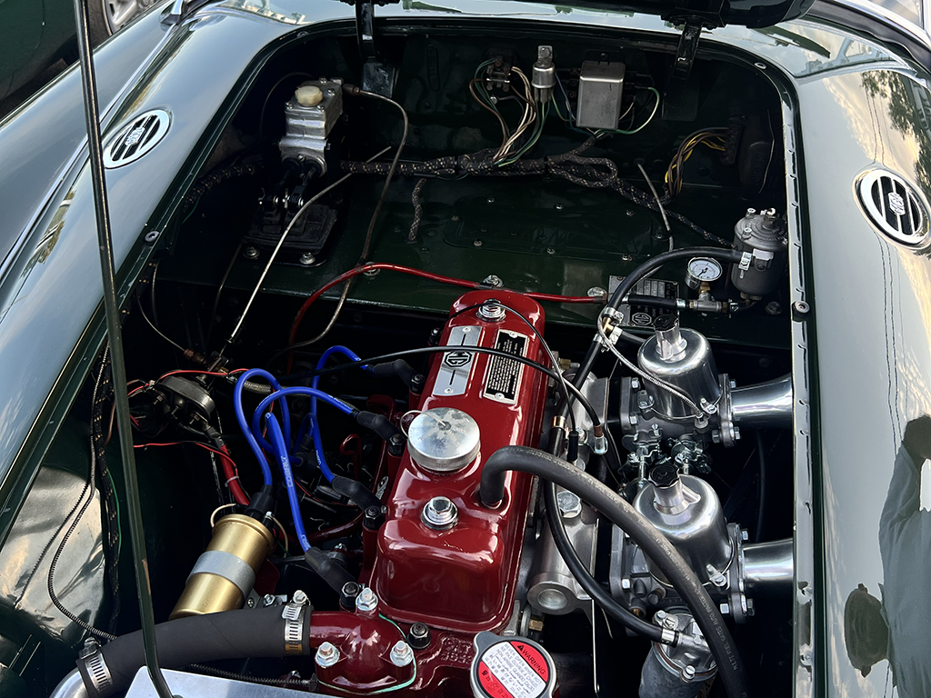 Inside view of a vintage car engine bay showing a red engine block, carburetors, and various engine components.