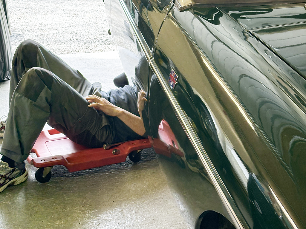 A person lying on a red creeper near a black car, inspecting the car's underside.