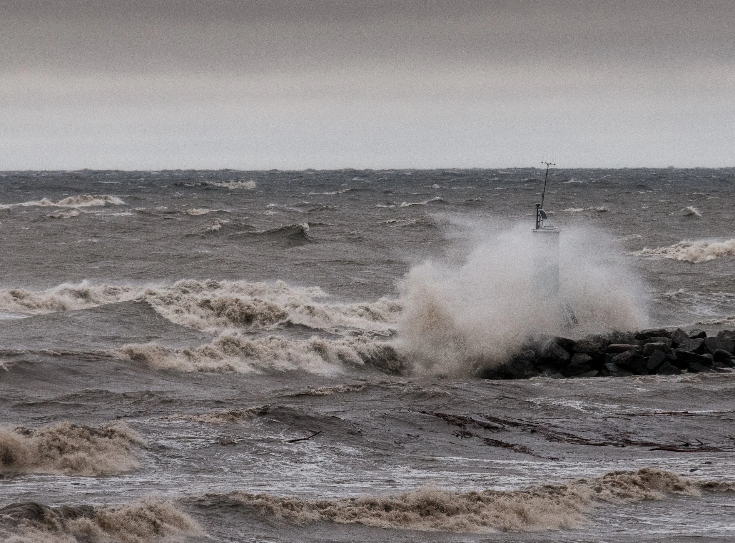 Stormy ocean with large waves crashing against rocks and a partially submerged navigation beacon.