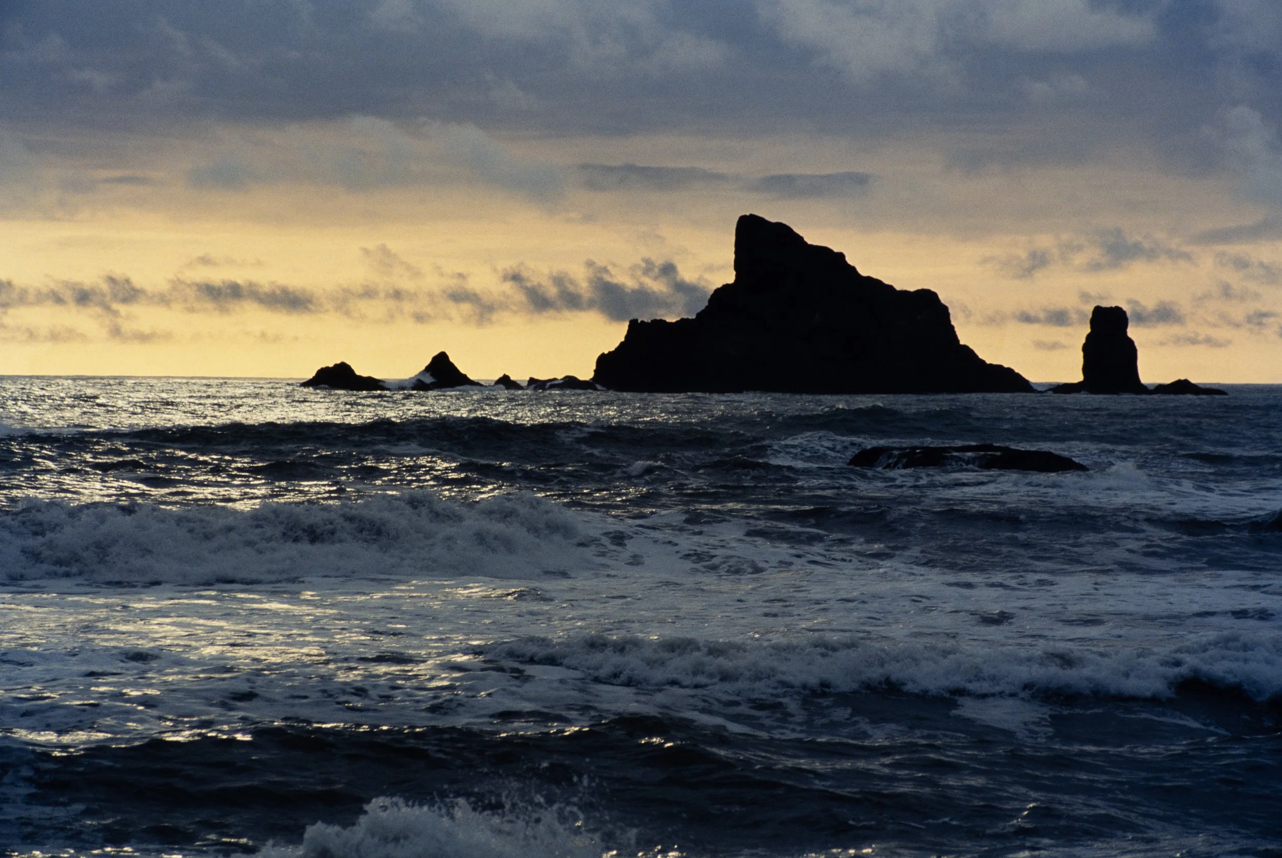 Sunset or sunrise over stormy ocean with dark silhouette of rocky islands and clouds in the sky.