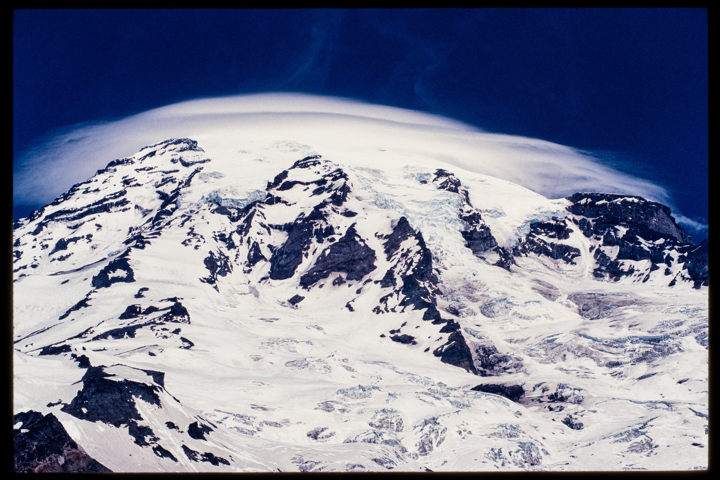 Snow-covered mountain peak under a dark blue sky with a cloud formation.