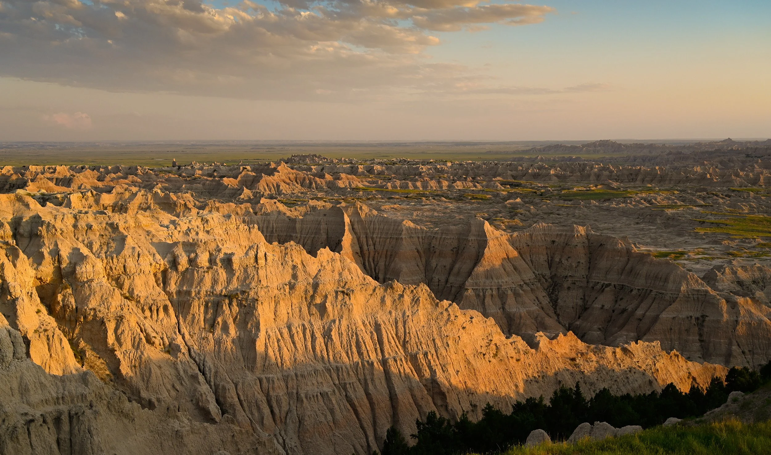 Sunset over the Badlands with rugged eroded rock formations and sparse vegetation.