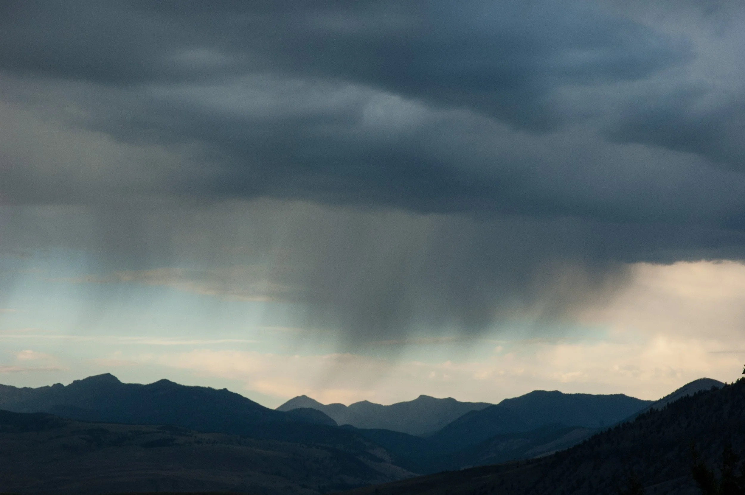 Dark storm clouds over mountain ranges with rain falling in the distance.