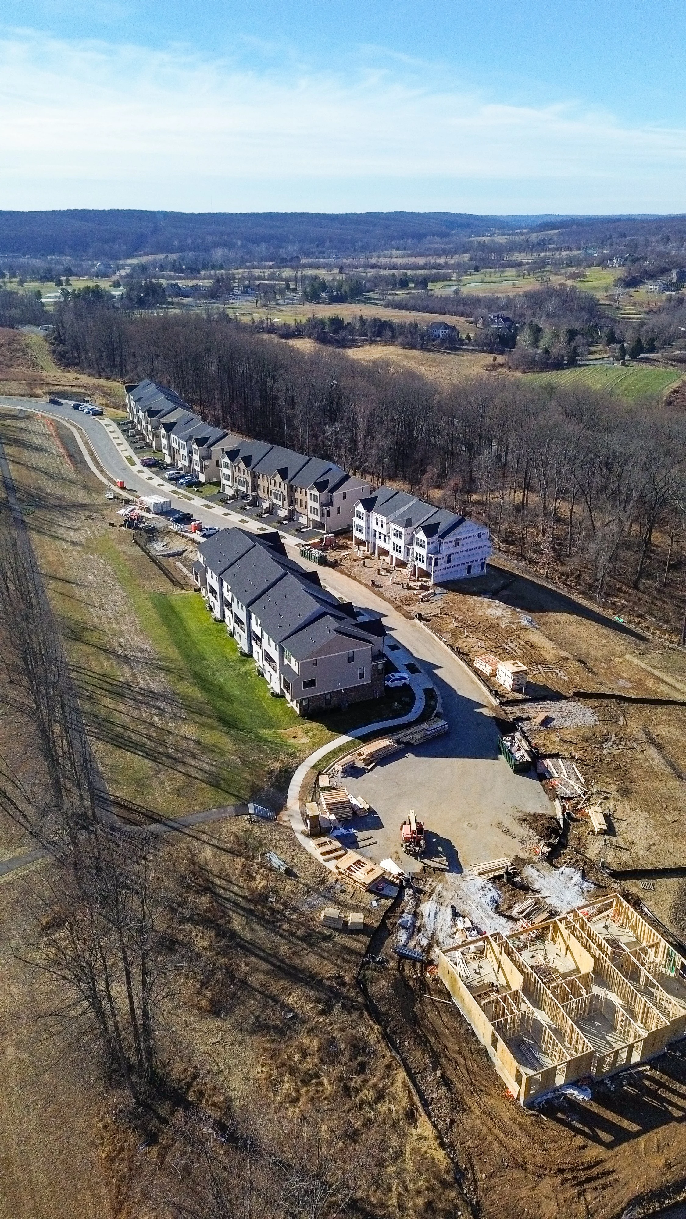 An aerial view of a construction site with newly built townhouses, with some houses still under construction, along with construction materials and equipment.
