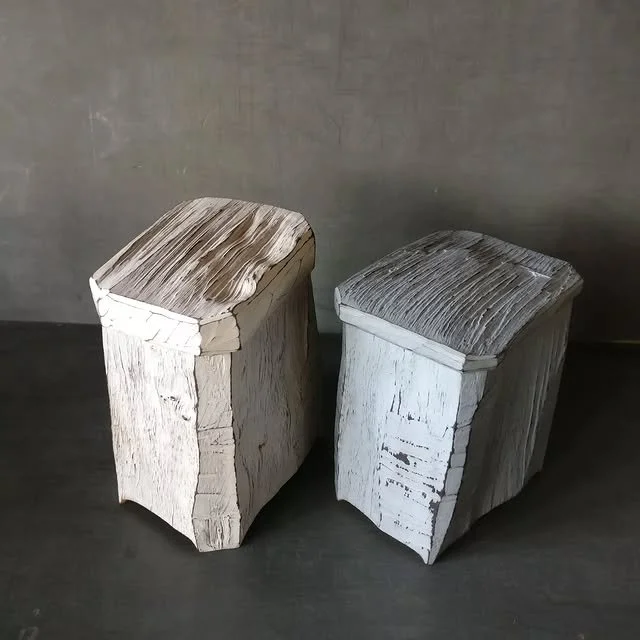 Zwei alte Holzkisten, die nebeneinander stehen, eine vor der anderen, auf einem dunklen Boden vor einer grauen Wand.