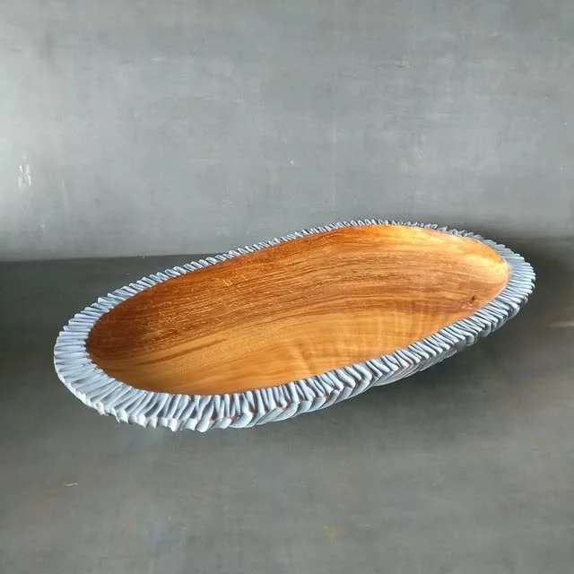Ein ovaler Holzschale mit einem silbernen, gewellten Rand auf einer grauen Oberfläche.