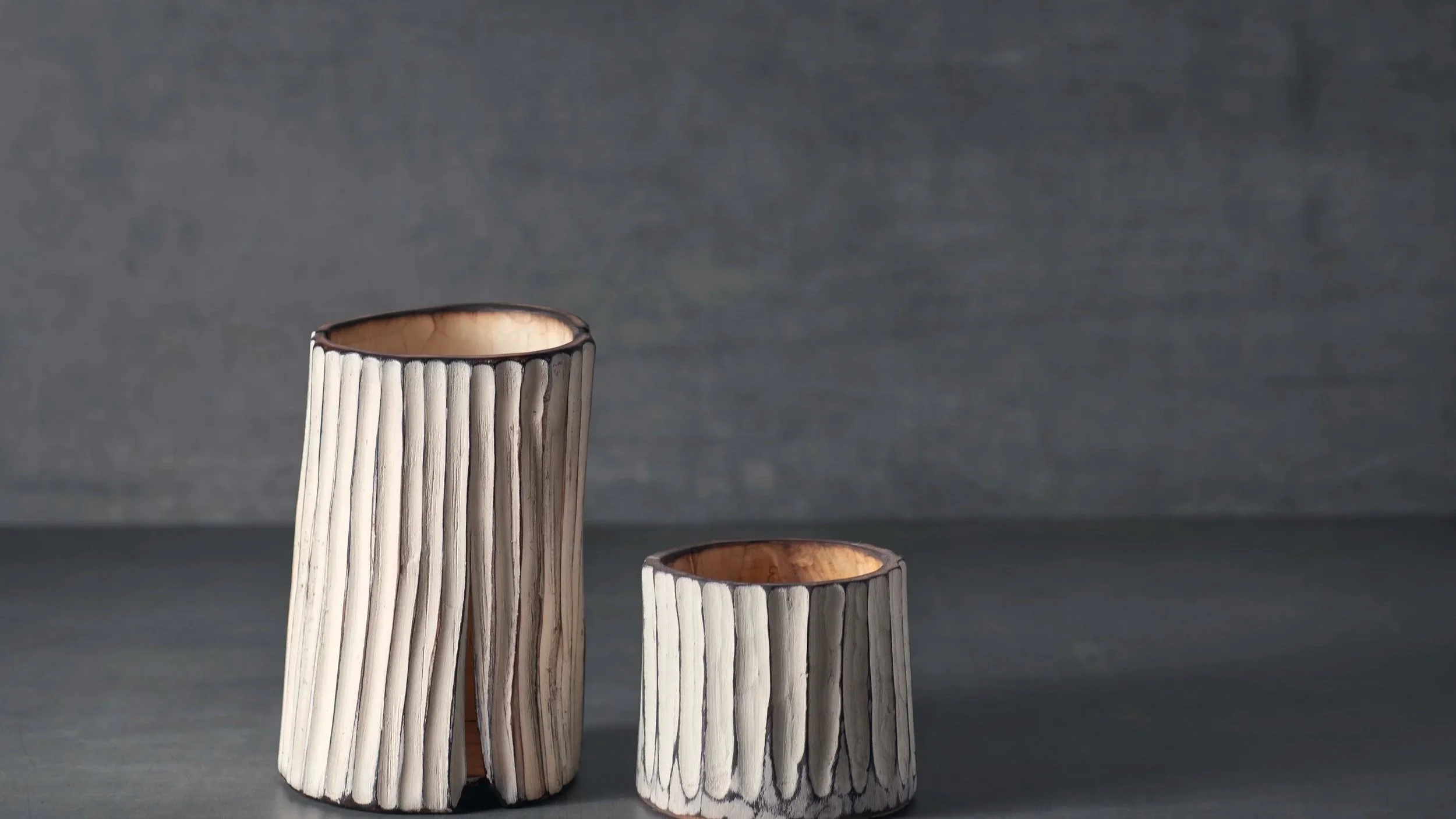 Zwei handgefertigte Kerzenhalter aus Holz, mit vertikalen Linien, vor grauem Hintergrund.