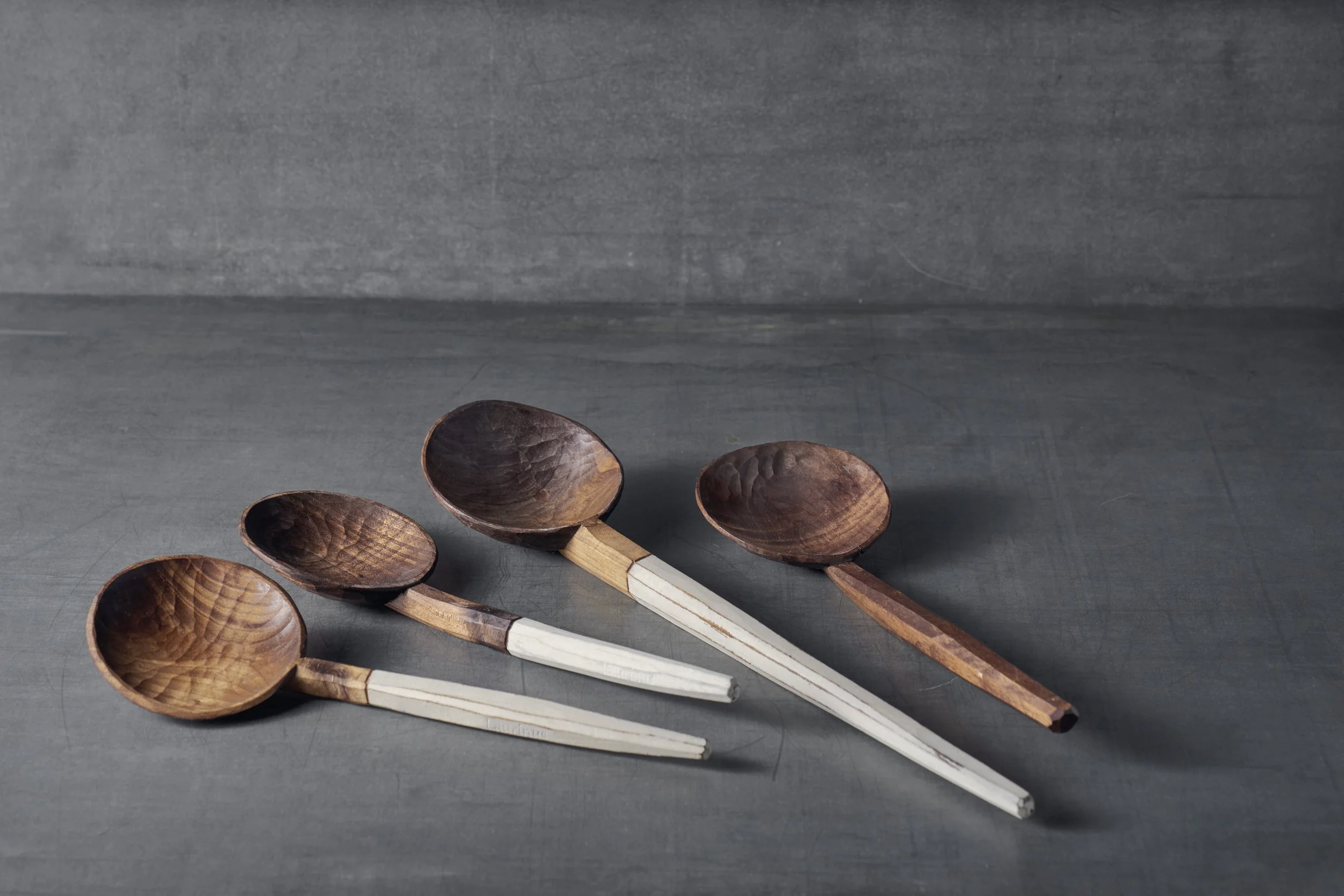 Vier handgeschnitzte Holzlöffel, die auf einer grauen Oberfläche liegen.