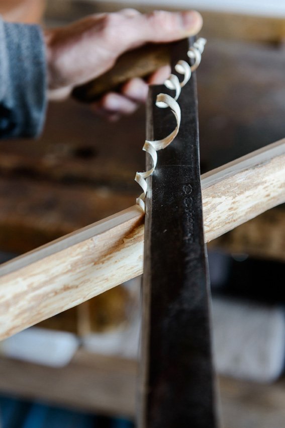 Eine Person schabt Holz mit einem Handhobel, um dünne Holzspäne zu erzeugen.