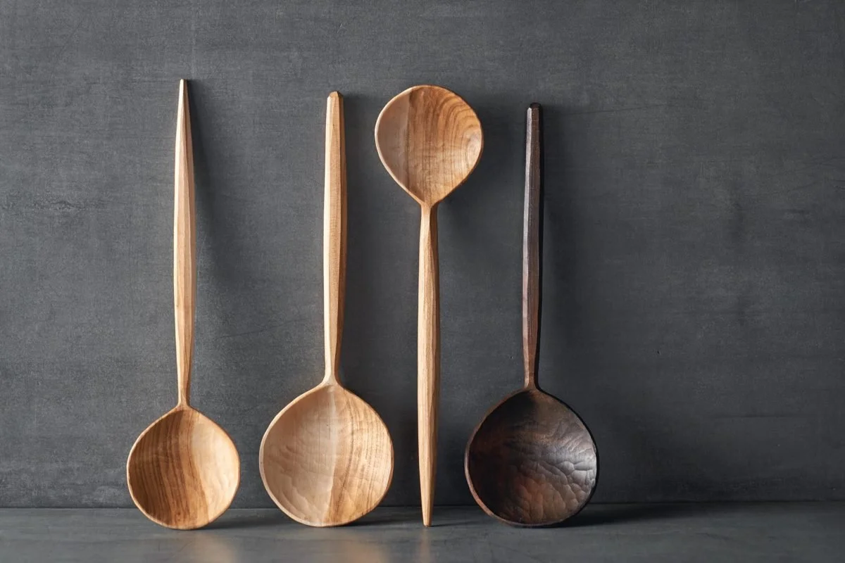 Vier hölzerne Esslöffel und -stäbchen, ein heller und ein dunkler, gegen eine dunkle Wand gestellt.