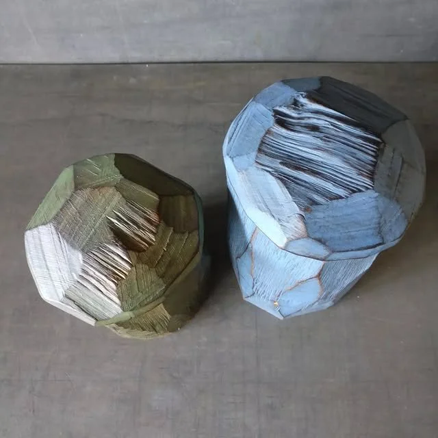 Zwei Holzstämme, eines grünlich und eines bläulich, auf einem Holzboden