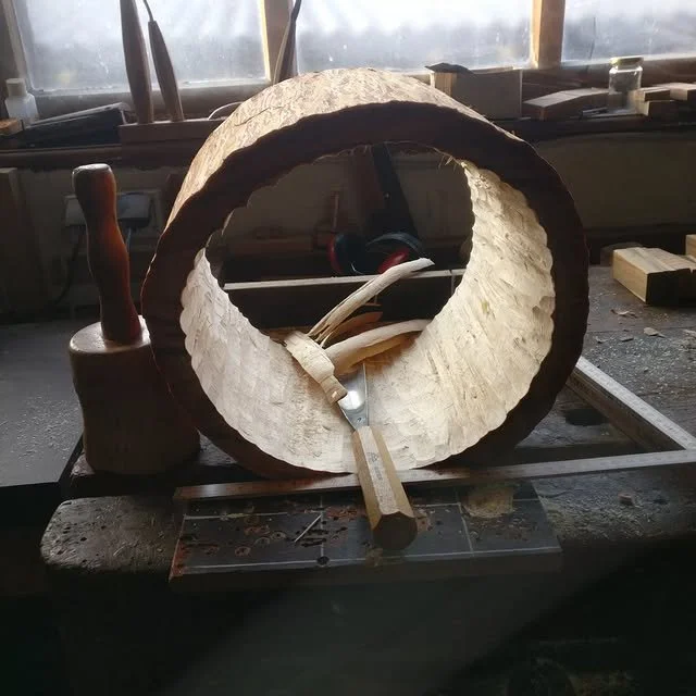 Holzspirale auf einer Werkbank, umgeben von Werkzeugen in einer Werkstatt.
