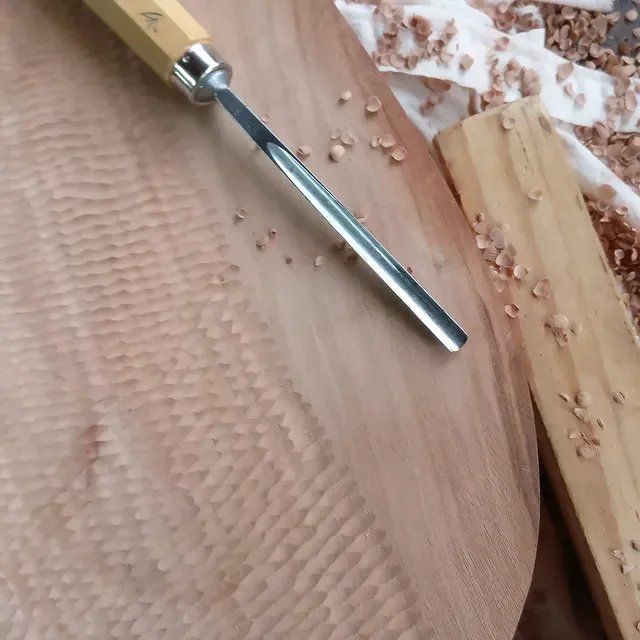 Holzarbeit mit Meißel und Holzreste auf einer Holzplatte.