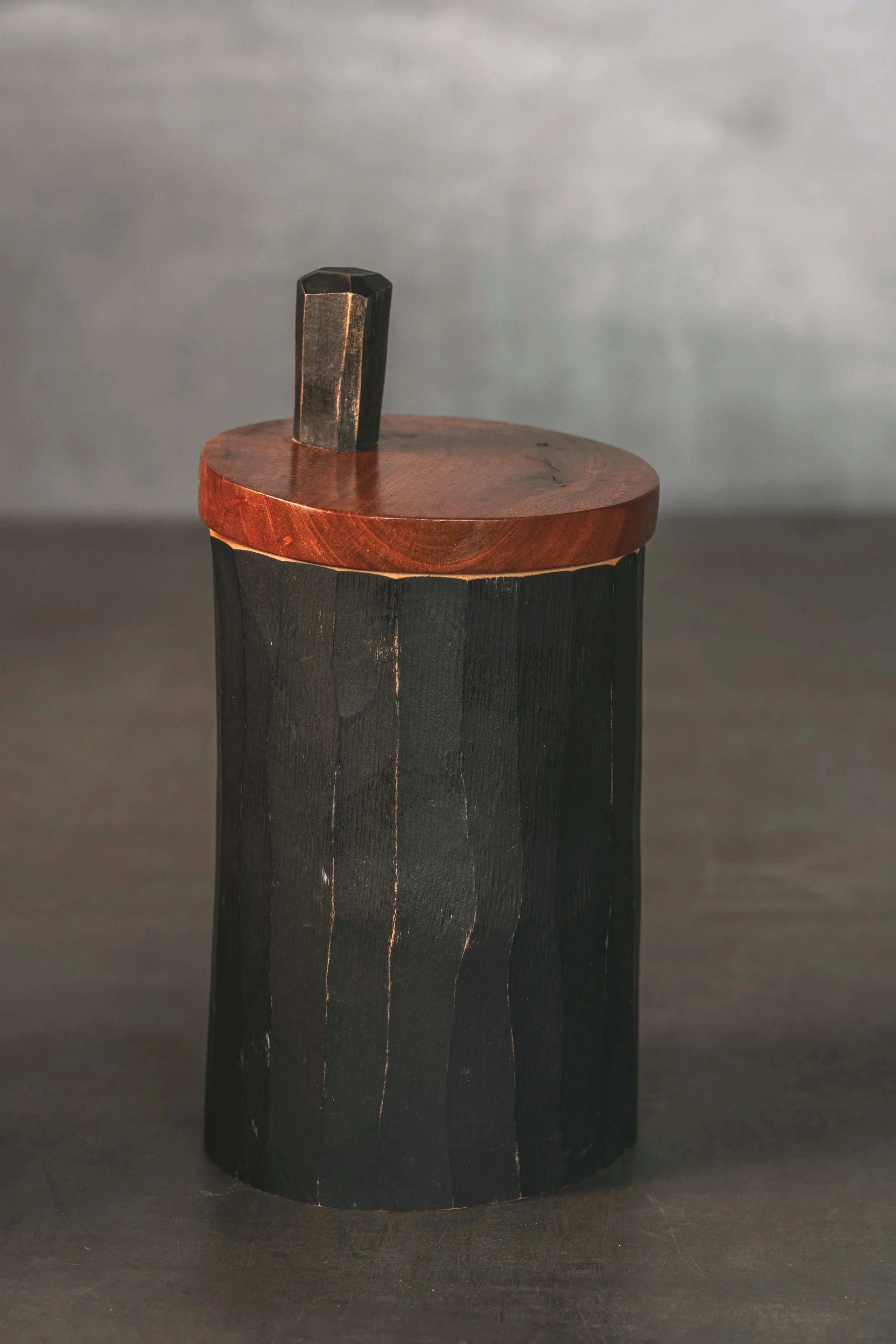 Ein Holzstück mit dunklem Holz und einer abgerundeten roten Oberseite, auf der ein dunkler Holzkeil steht.