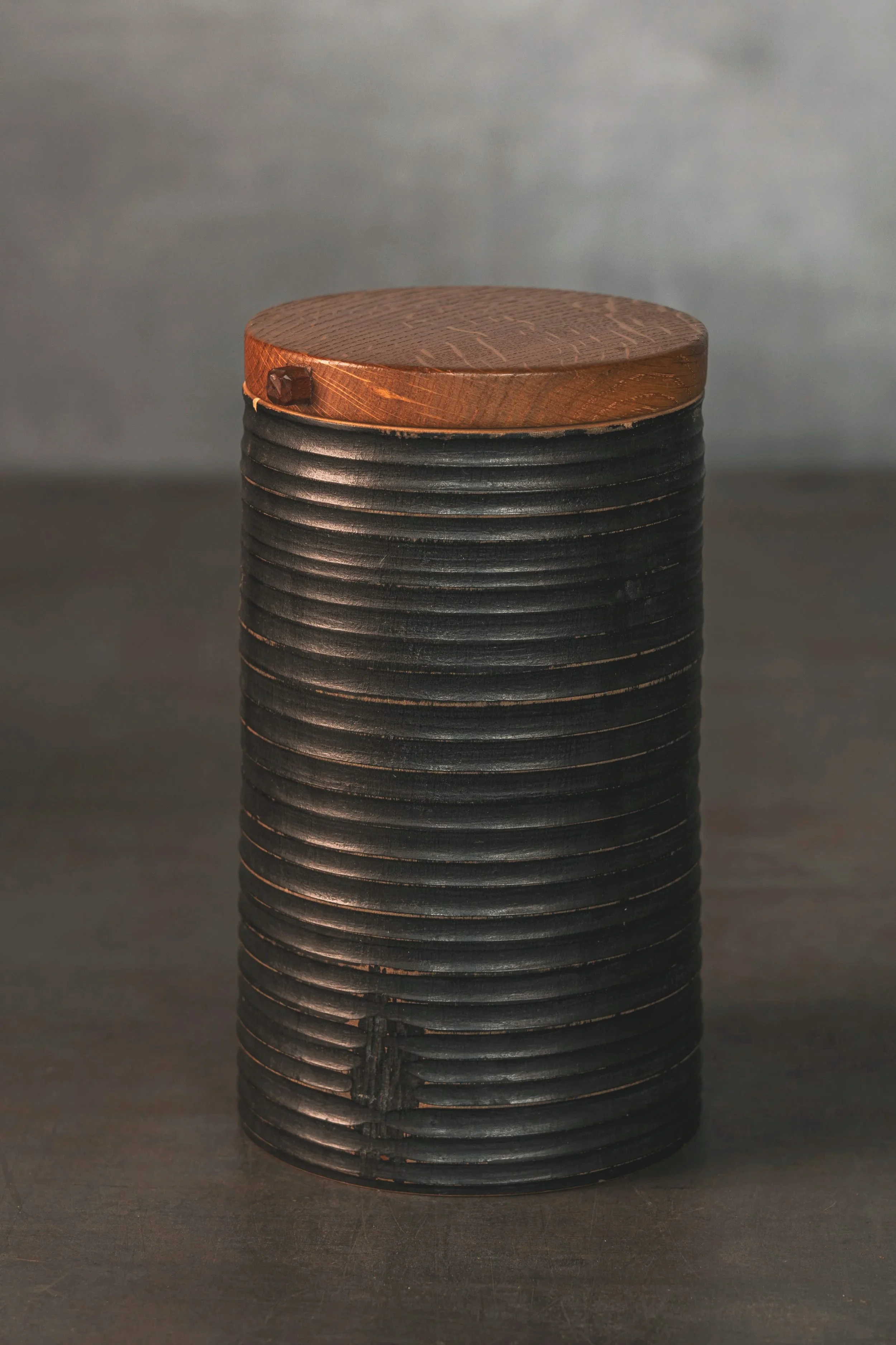 Zylindrische Holzdose. Oberfläche mit gedrechselten , horizontalen Rillen. Schwarz bemalt und poliert. Deckel aus rotbraunem Holz.