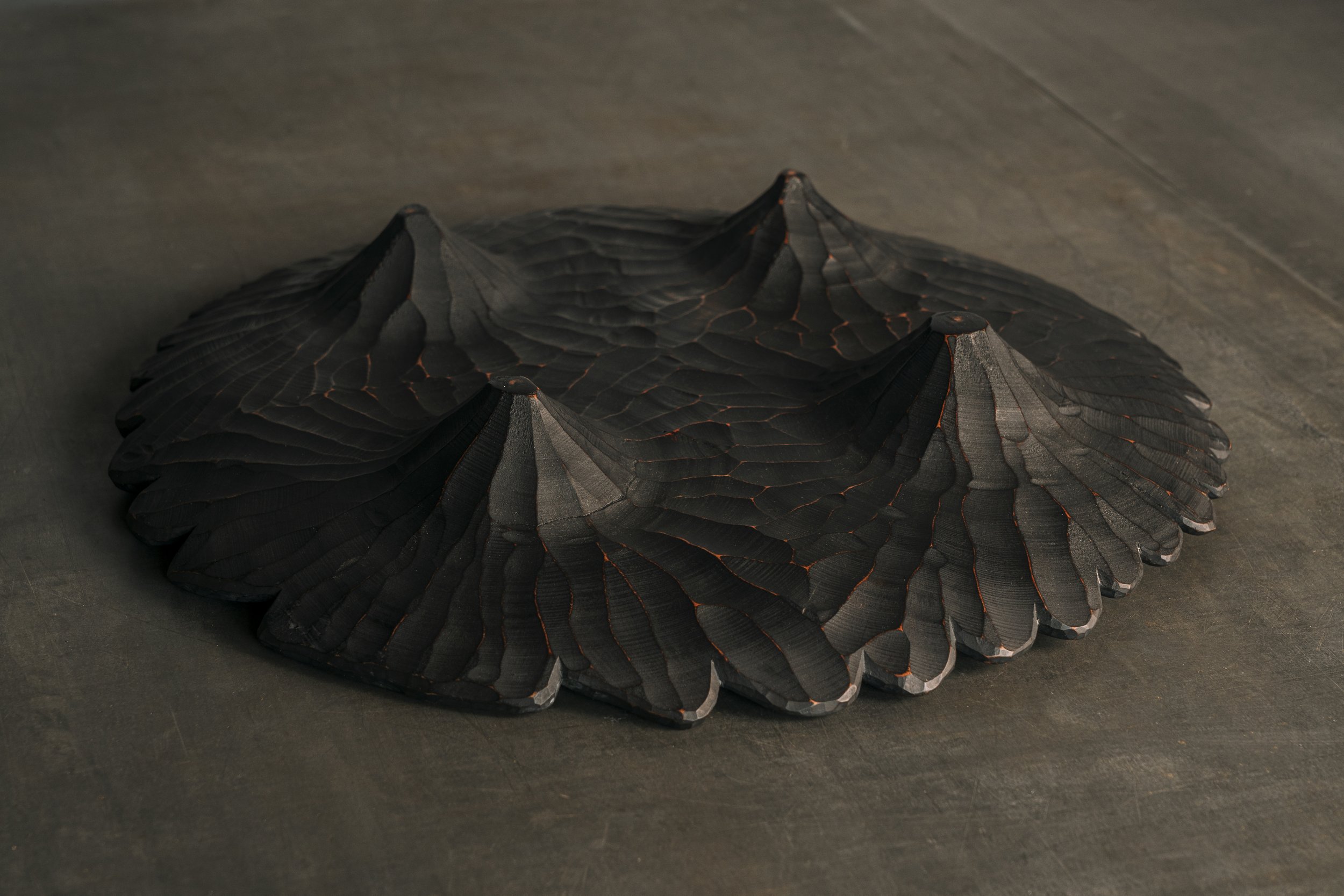 Unterseite einer flachen Holzschale mit vier Standfüßen.