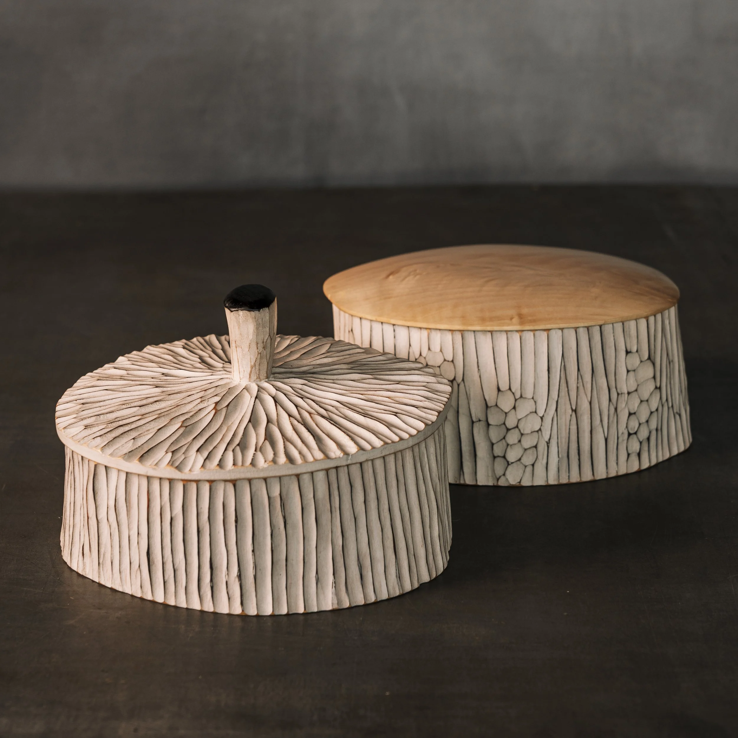 	

Zwei flache ,geschnitzte, weiß bemalte Holzdosen oder Urnen mit kanelierter Struktur.Eine mit einem Knauf auf dem Deckel, die andere mit glattem ,abgerundetem Deckel aus hellem Ahornholz. Verwendbar als Schmuckschachtel oder Keksdose.