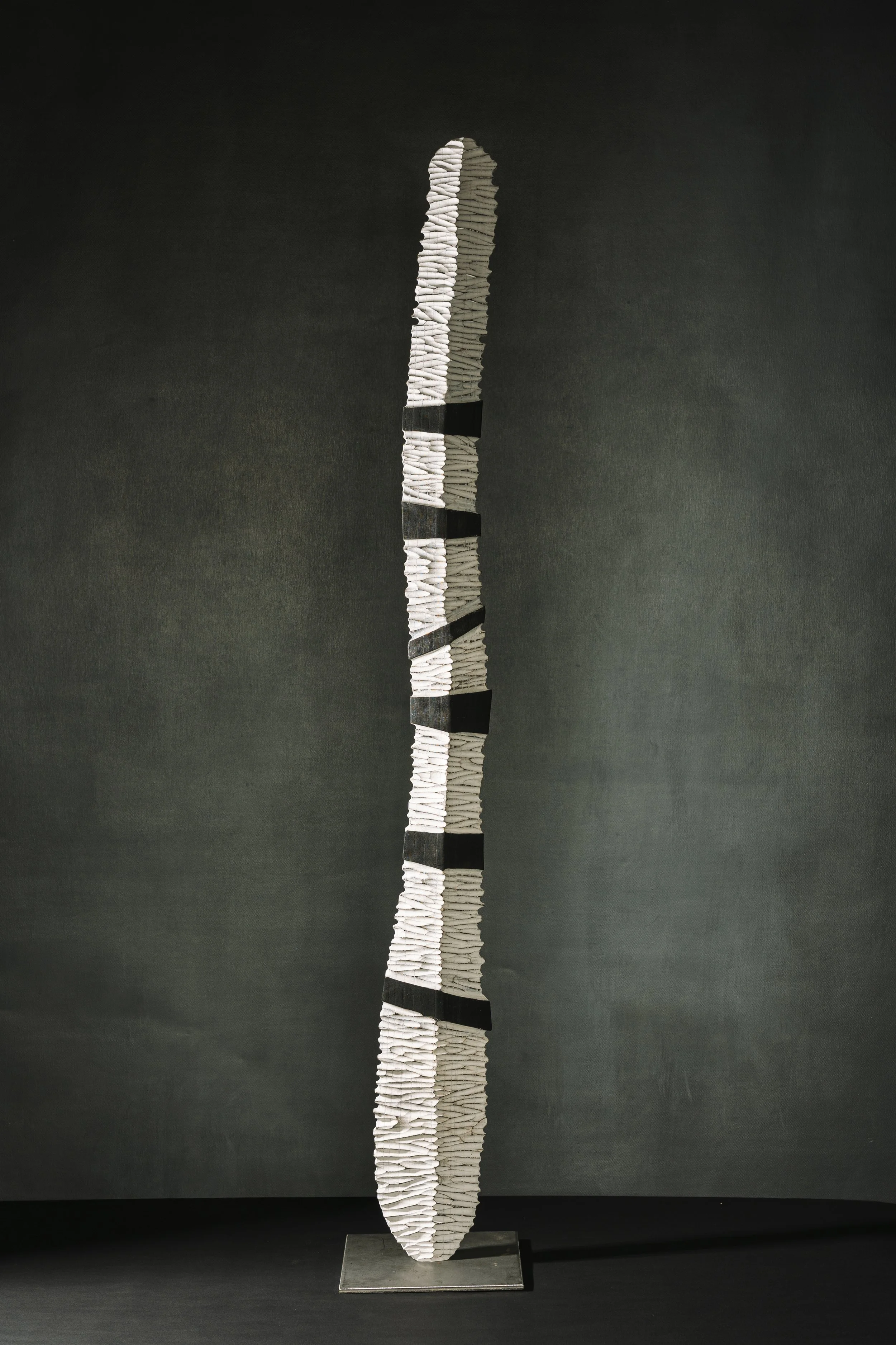 Stelenartige Skulptur aus Holz mit quergeriffelter Struktur und spannender Licht-Schattenwirkung.