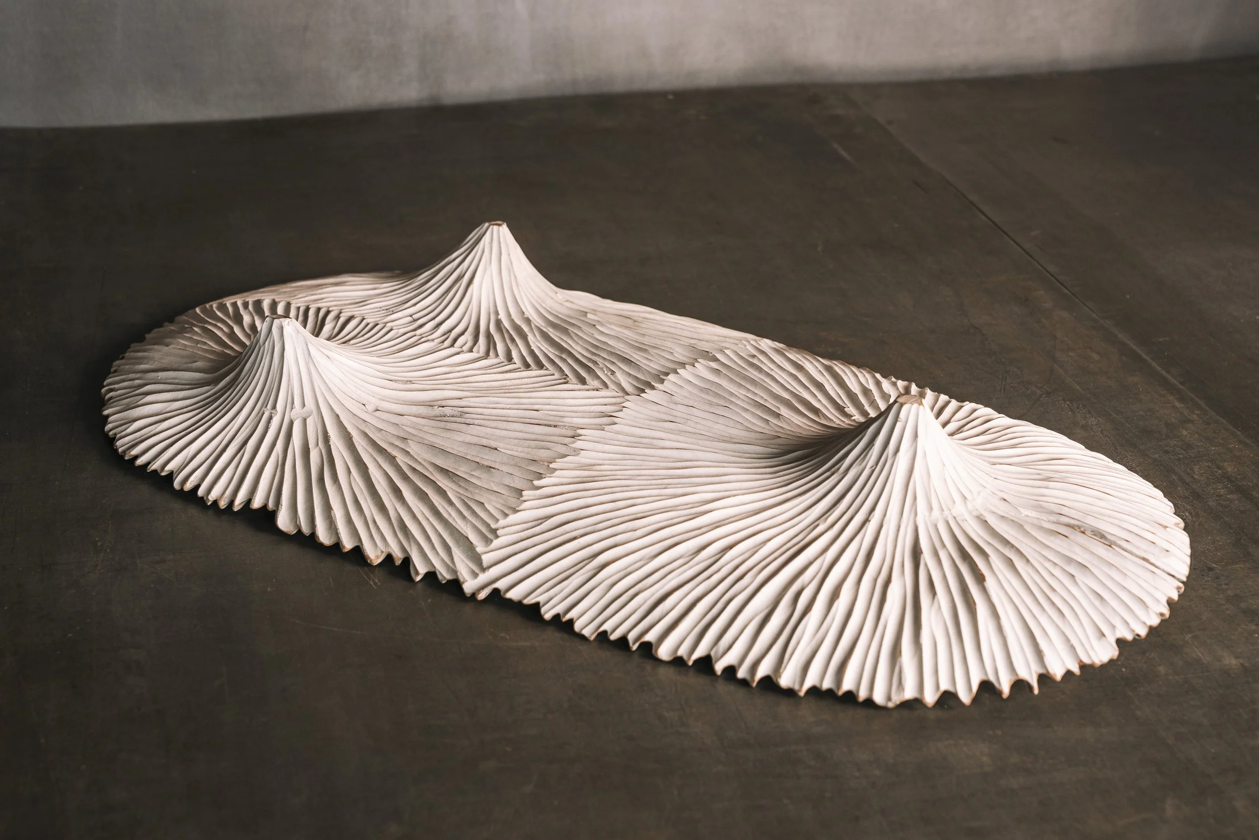 Skulptur aus weißem, gefaltetem Material, das wie eine Bergkette mit drei Gipfeln aussieht, auf einer dunklen Oberfläche liegend.