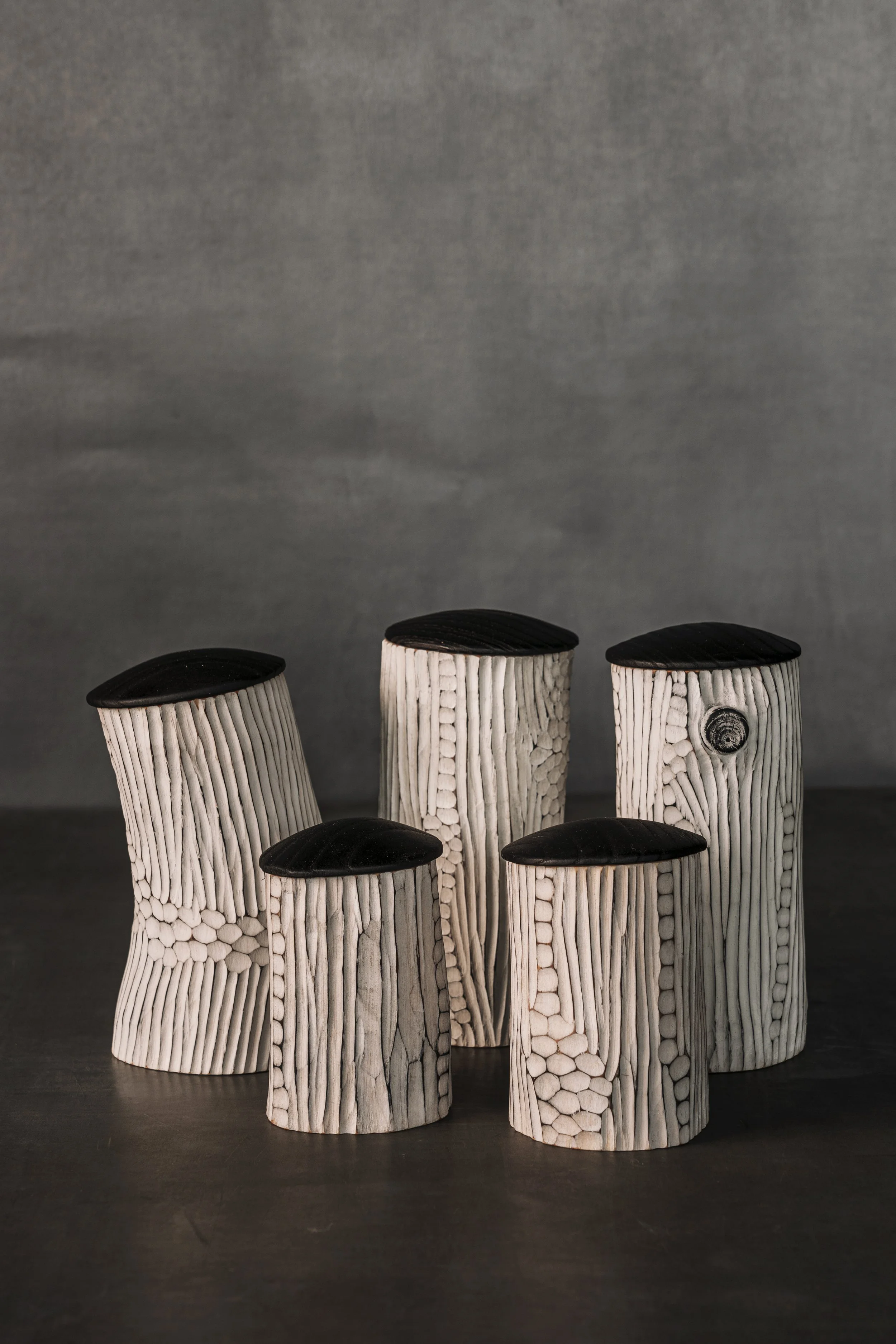 Serie bestehend aus aus fünf geschnitzten Holzdosen von Laurin Kause. 
Wandung weiß bemalt und mit textur beschnitzt. Deckel aus schwarz gebranntem Eschenholz. Shrinkpots.