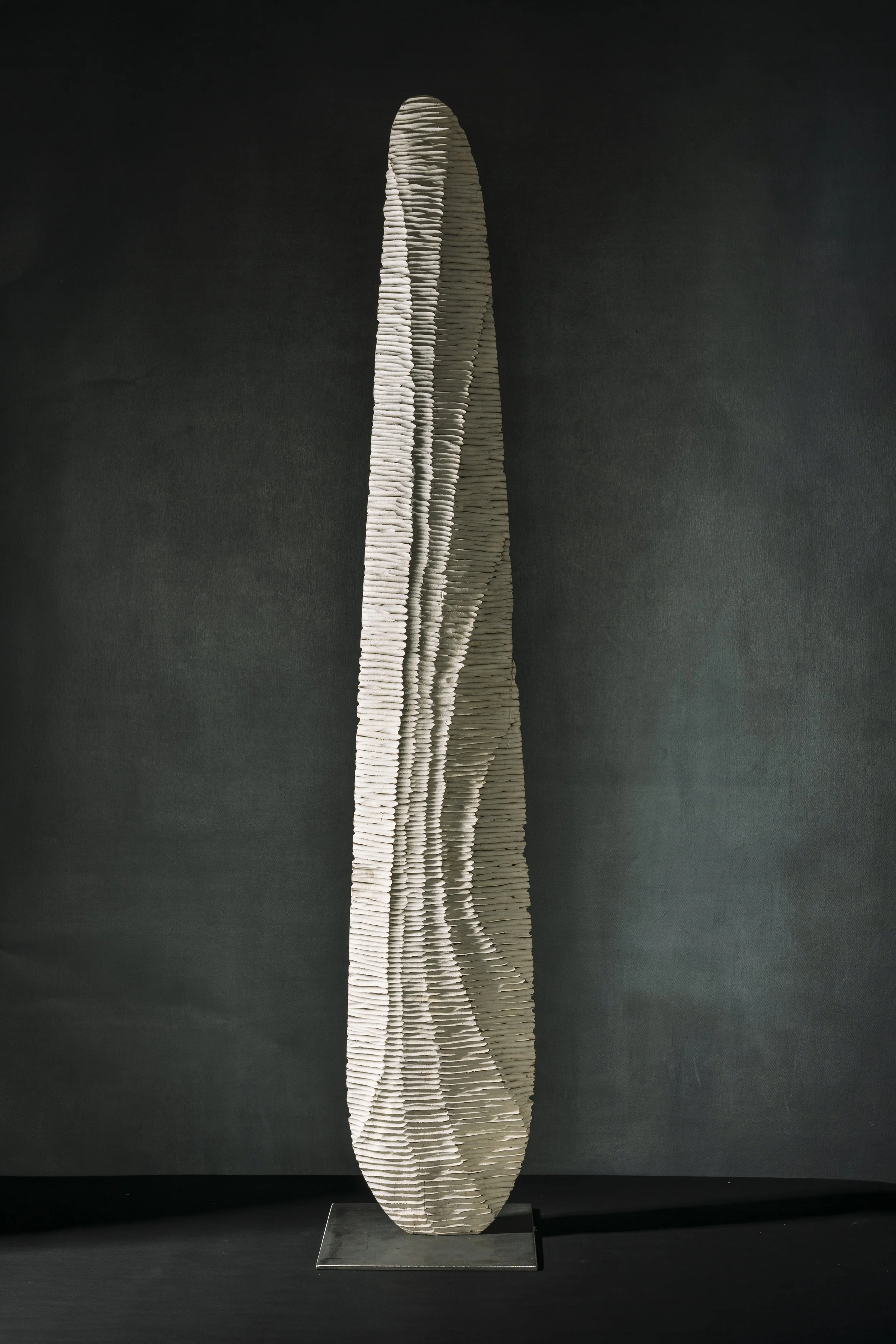 Skulptur aus weißen, schichtartigen Elementen, die eine elegante, geschwungene Form bildet, auf einem schwarzen Hintergrund.