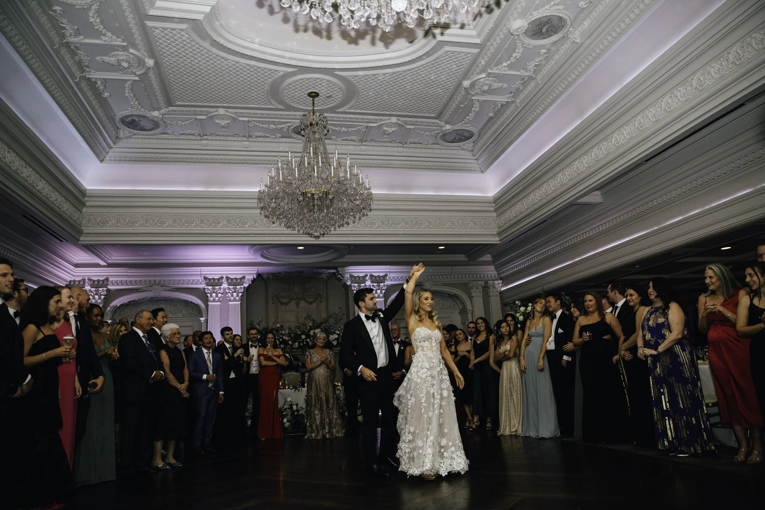 A bride and groom dancing at their wedding reception surrounded by guests in an ornate, chandelier-lit ballroom.  New York City Jewish wedding photographer