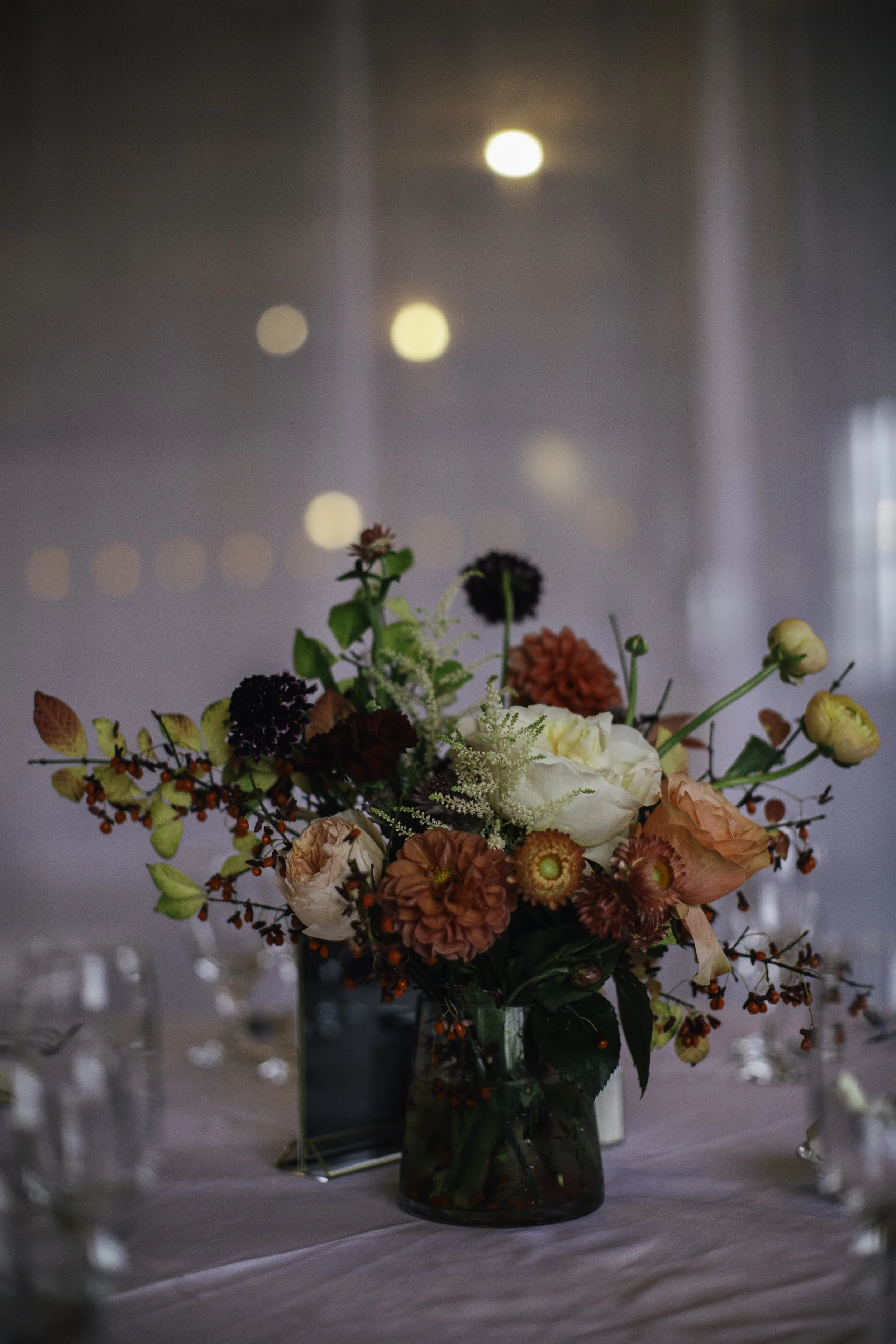 A floral arrangement in a glass vase on a table with blurred background and soft lighting.
