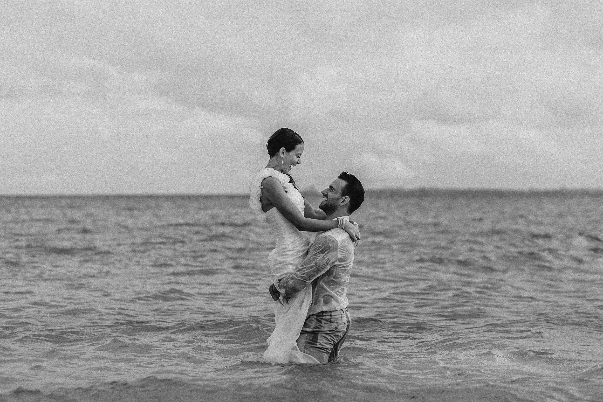 A man holding a woman in his arms in the ocean. NYC destination wedding photographer