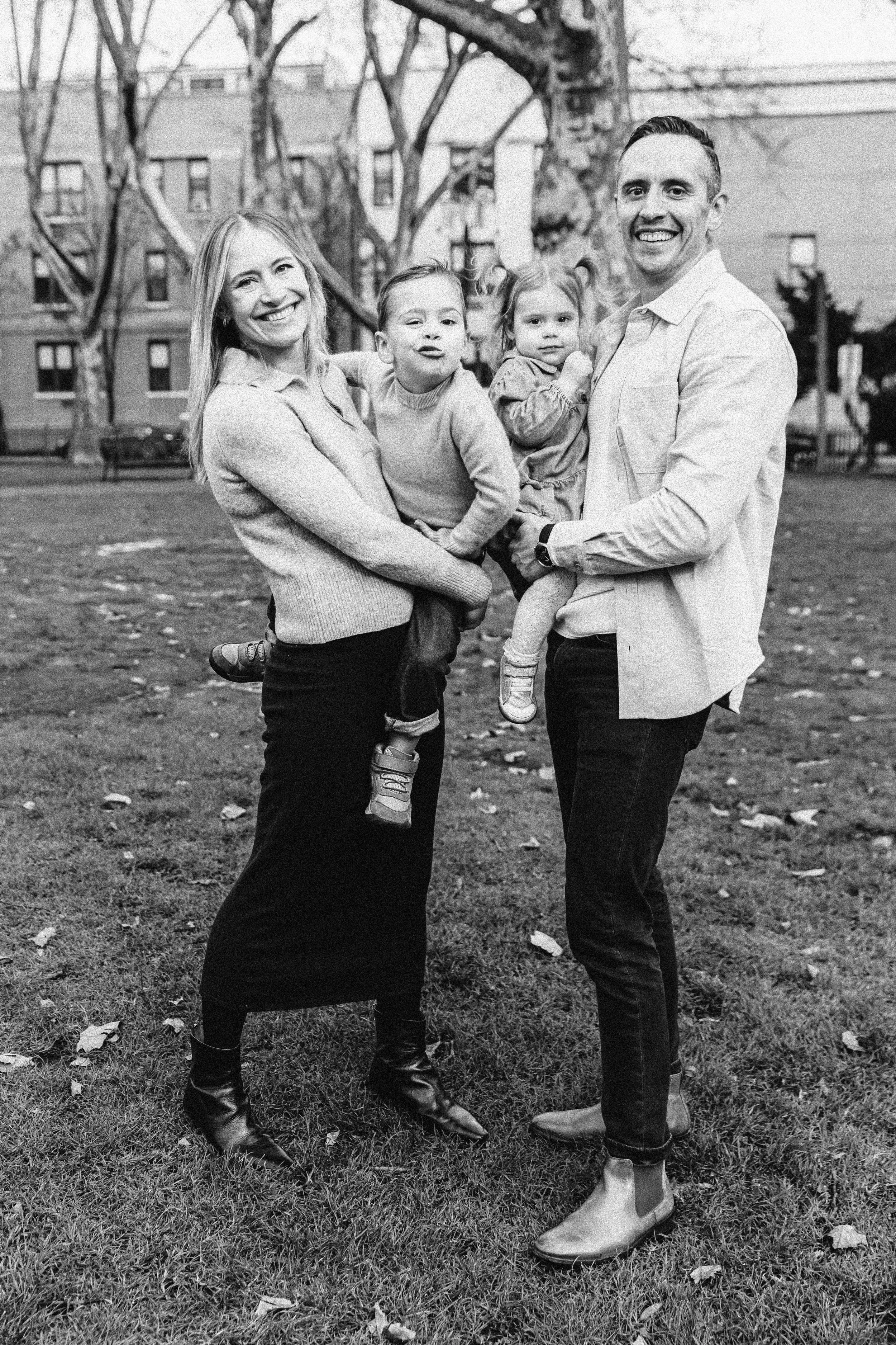 Family of four standing on grass in park with trees — NYC family photography