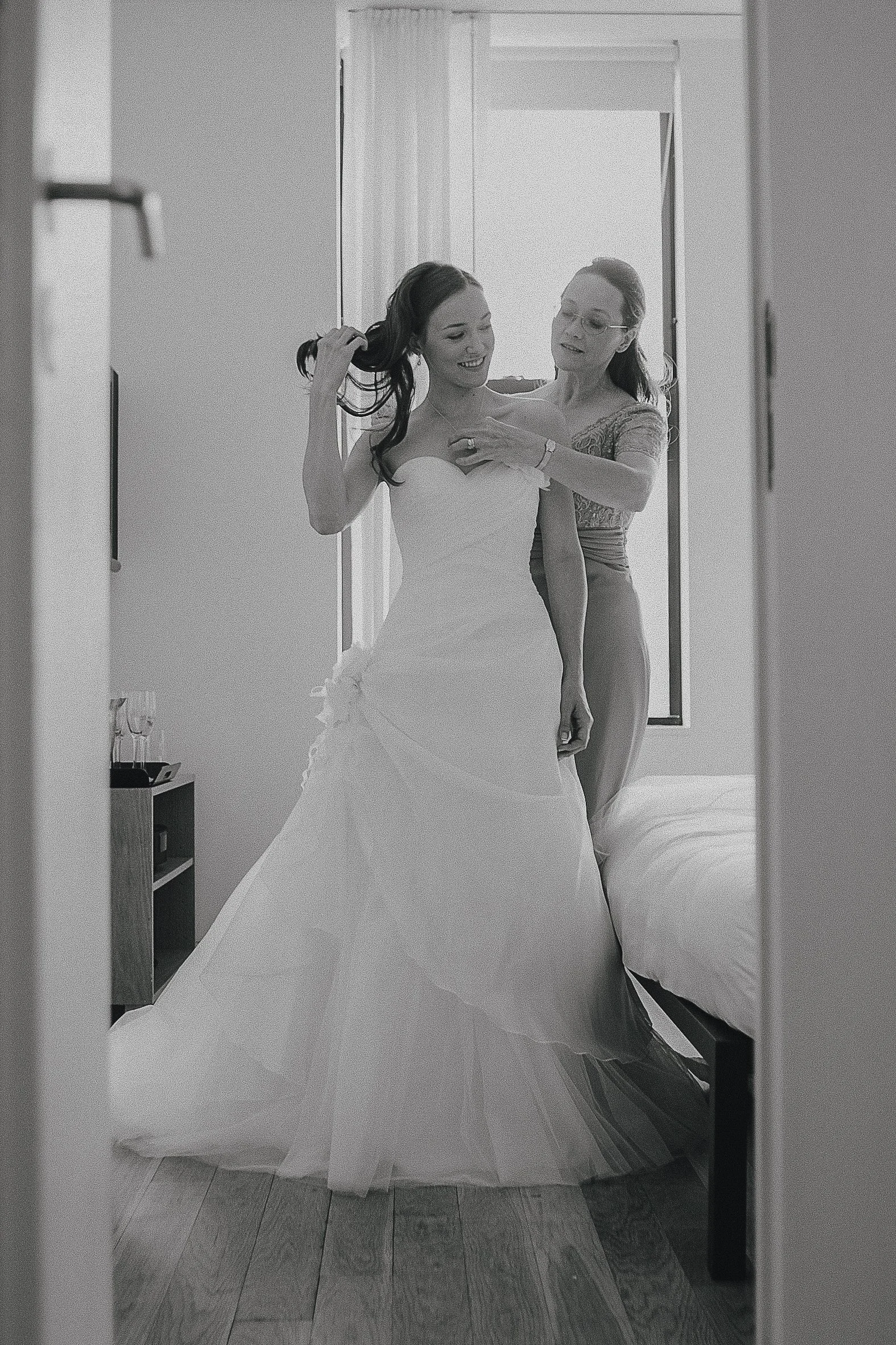 A bride getting ready with help from a woman, possibly a bridesmaid, in a room with a window. New York City wedding photographer