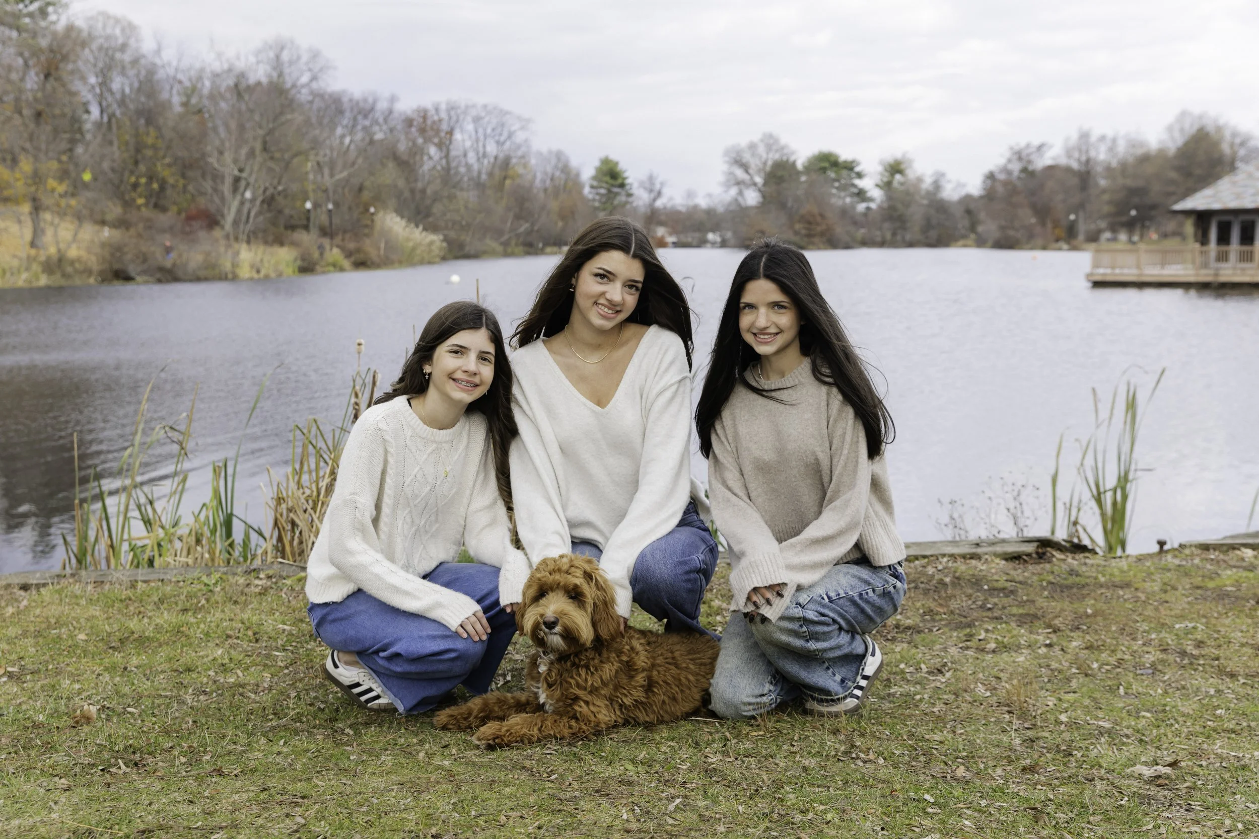 Three girls and dog sitting by lake with fall foliage — family lifestyle photography in NYC